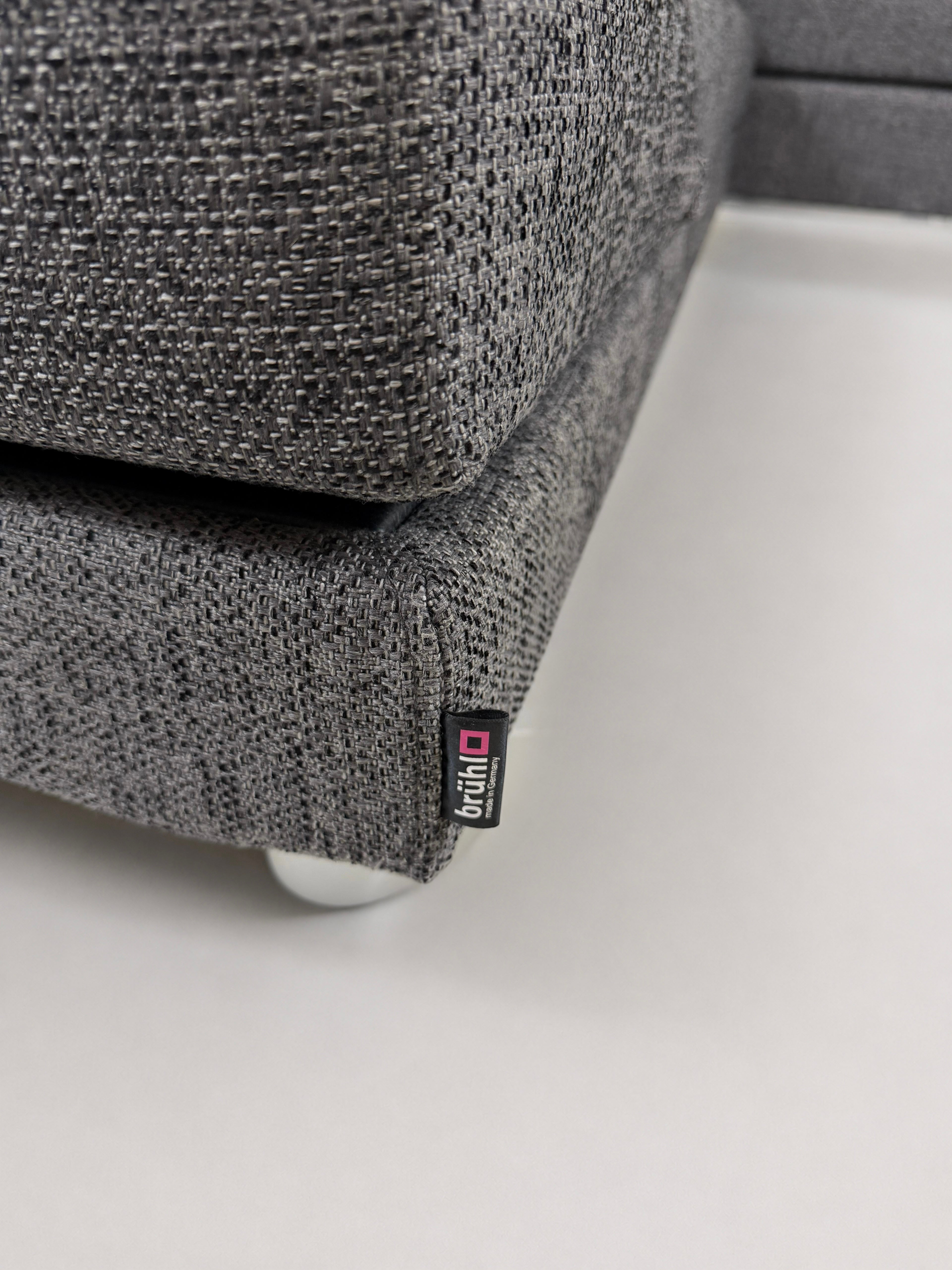 Gebrauchtes graues Brühl Four Two Designer Stoff Sofa vor einer Wand, stilvoll und modern eingerichtet.