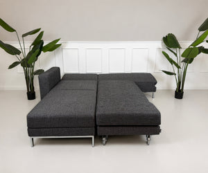 Gebrauchtes graues Brühl Four Two Designer Stoff Sofa vor einer Wand, stilvoll und modern eingerichtet.