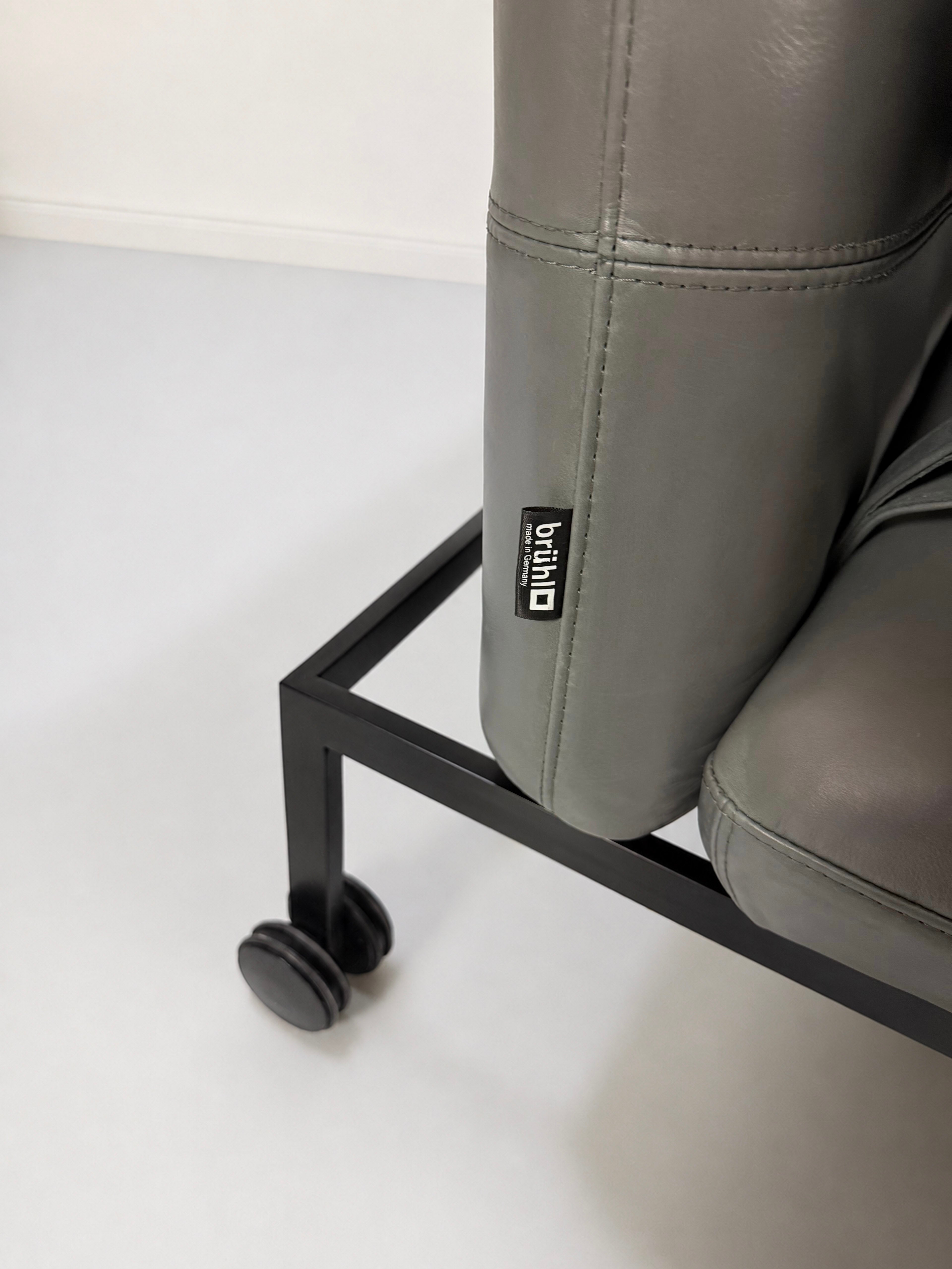 Gebrauchter grauer Brühl Roro Designer Leder Longchair vor einer Wand, stilvoll und modern eingerichtet.