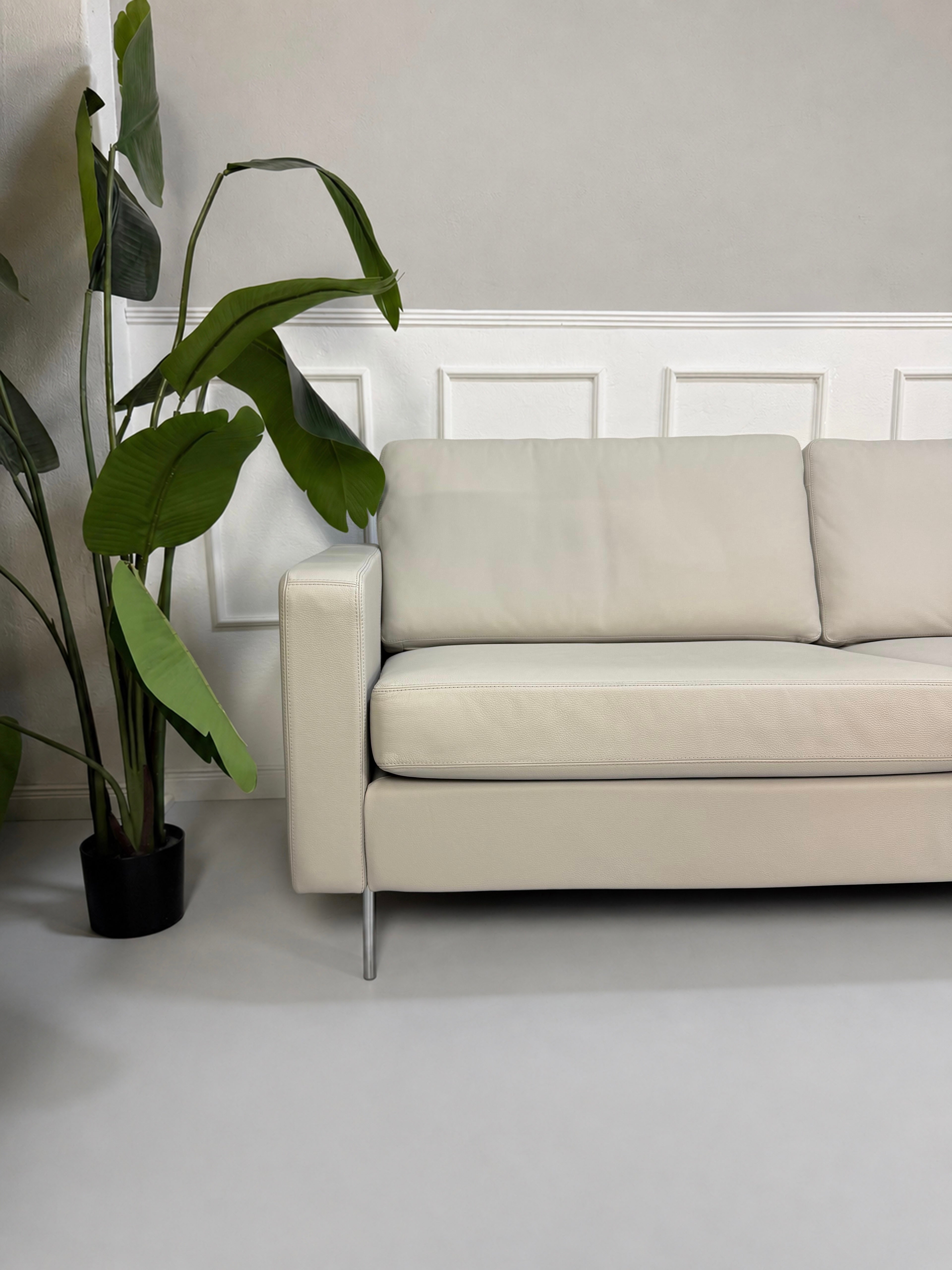 Gebrauchtes graues COR Conseta Designer Leder Sofa vor einer Wand, stilvoll und modern eingerichtet.