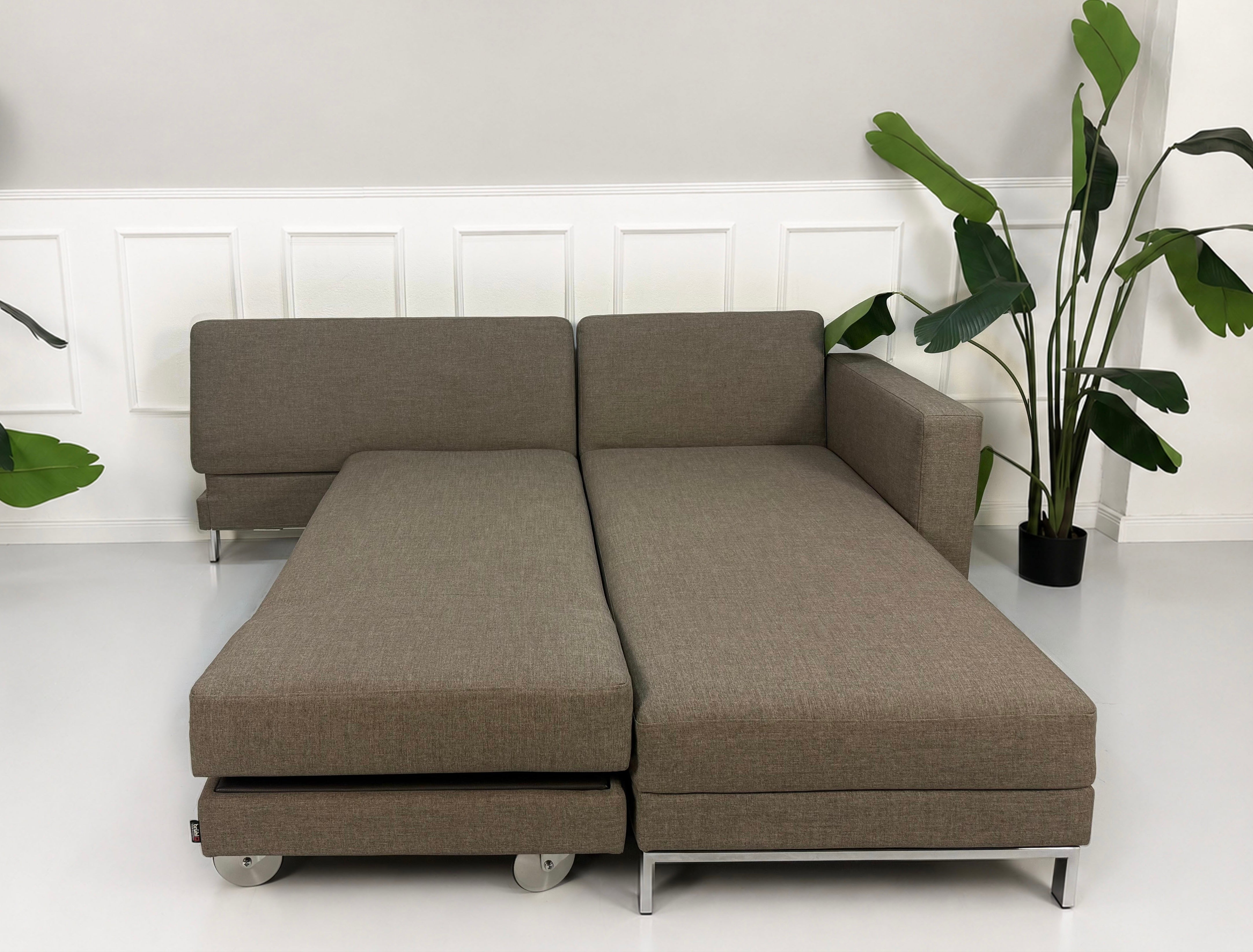 Gebrauchtes braunes Brühl Fourtwo Designer Stoff Sofa vor einer Wand, stilvoll und modern eingerichtet.