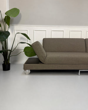 Gebrauchtes braunes Brühl Fourtwo Designer Stoff Sofa vor einer Wand, stilvoll und modern eingerichtet.