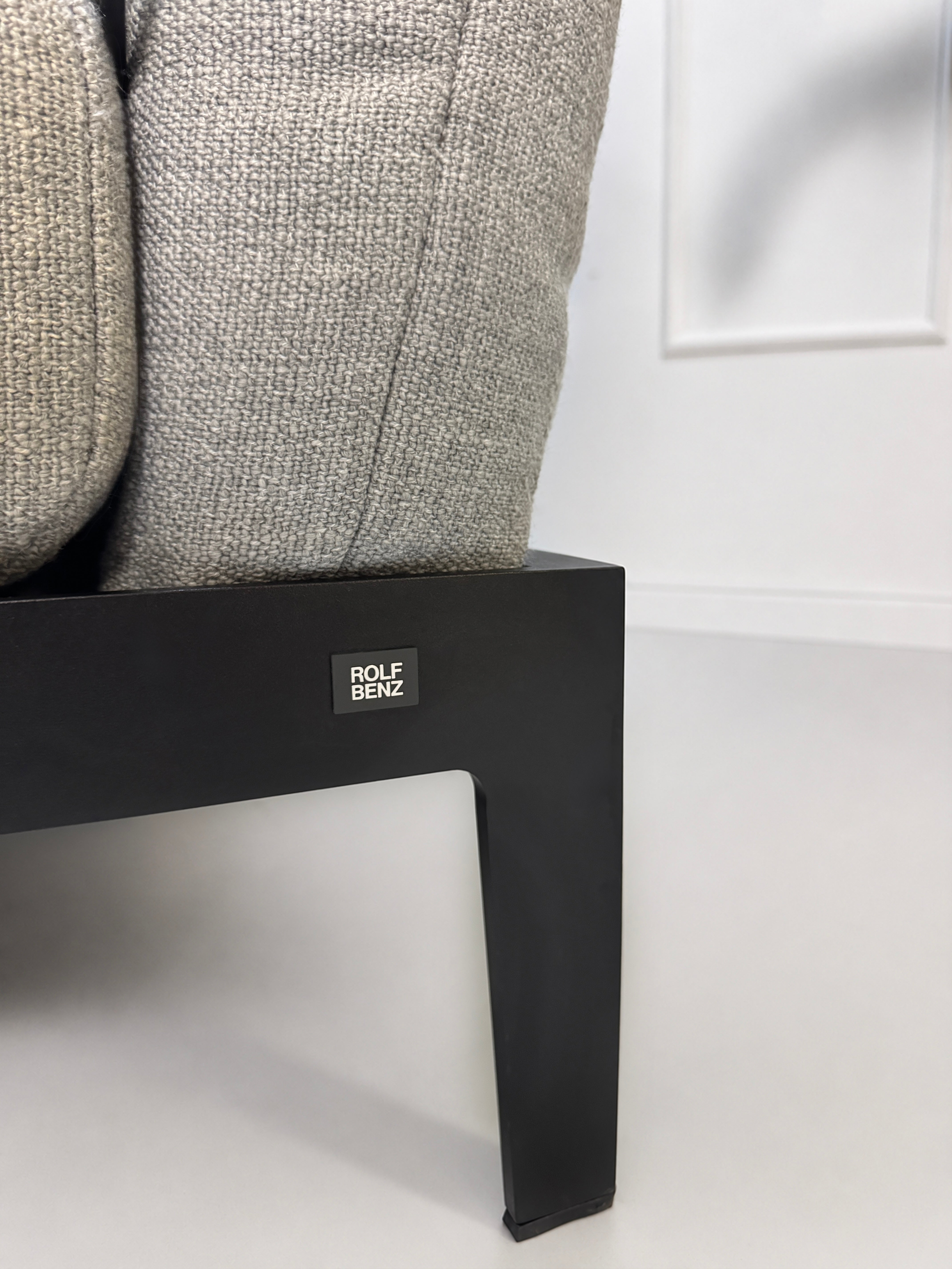 Gebrauchtes graues Rolf Benz Mera Designer Stoff Sofa vor einer Wand, stilvoll und modern eingerichtet.