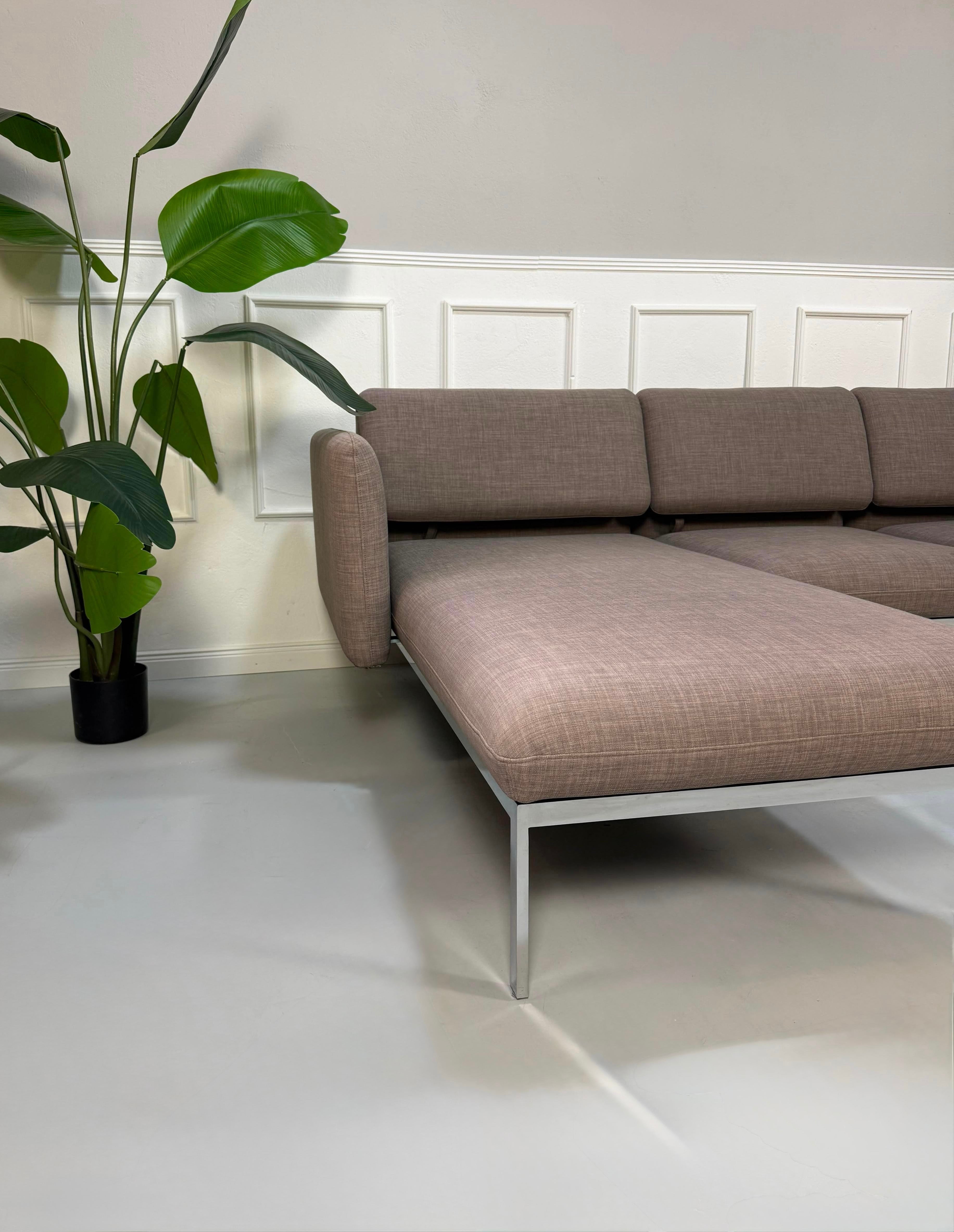 Gebrauchtes graues Brühl Roro Designer Stoff Ecksofa vor einer Wand, stilvoll und modern eingerichtet.