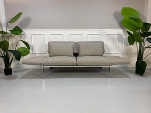 Fabrikverkauf Brühl Roro Designer Stoff Sofa vor einer Wand, stilvoll und modern eingerichtet.