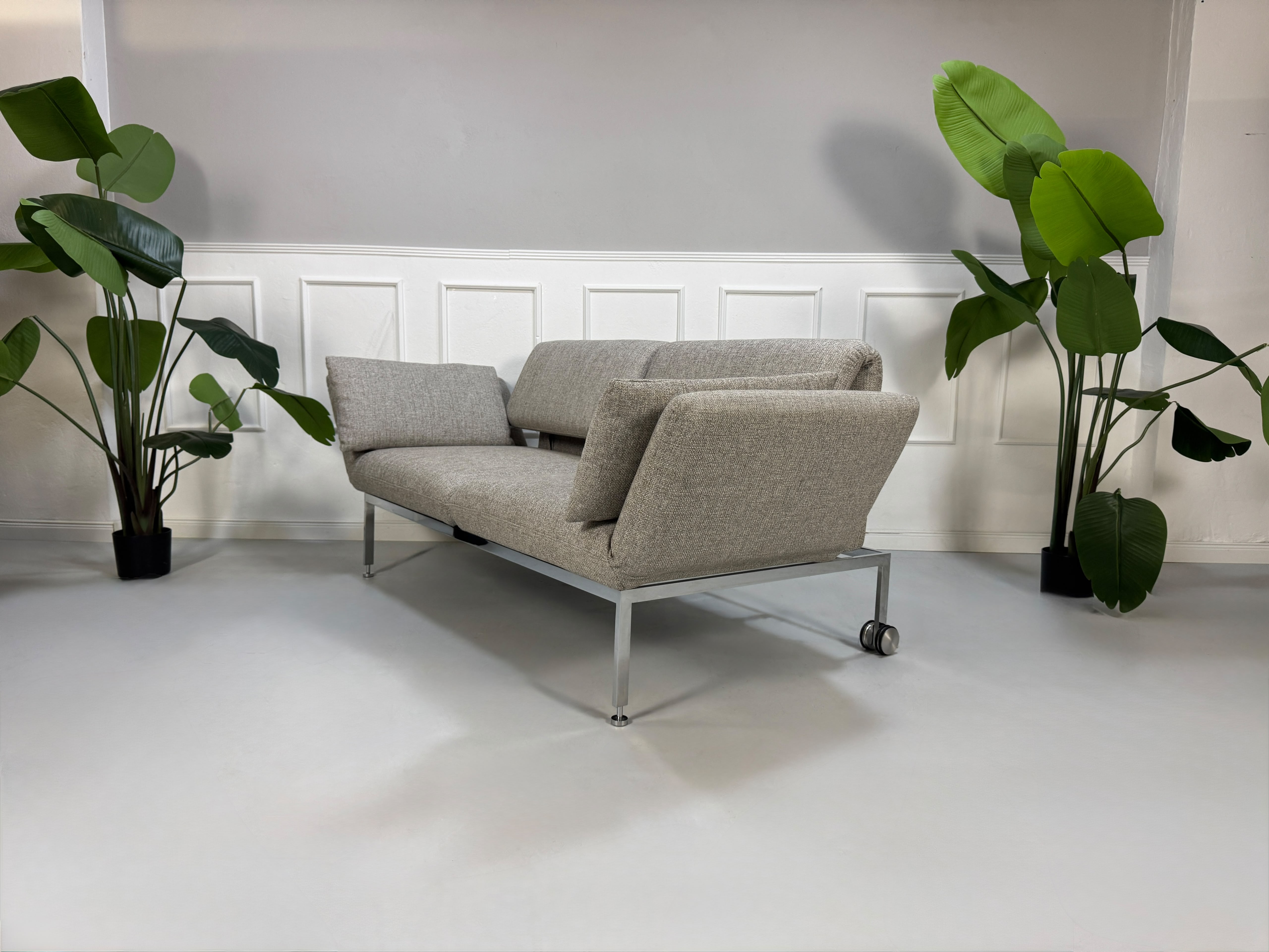Fabrikverkauf Brühl Roro Designer Stoff Sofa vor einer Wand, stilvoll und modern eingerichtet.