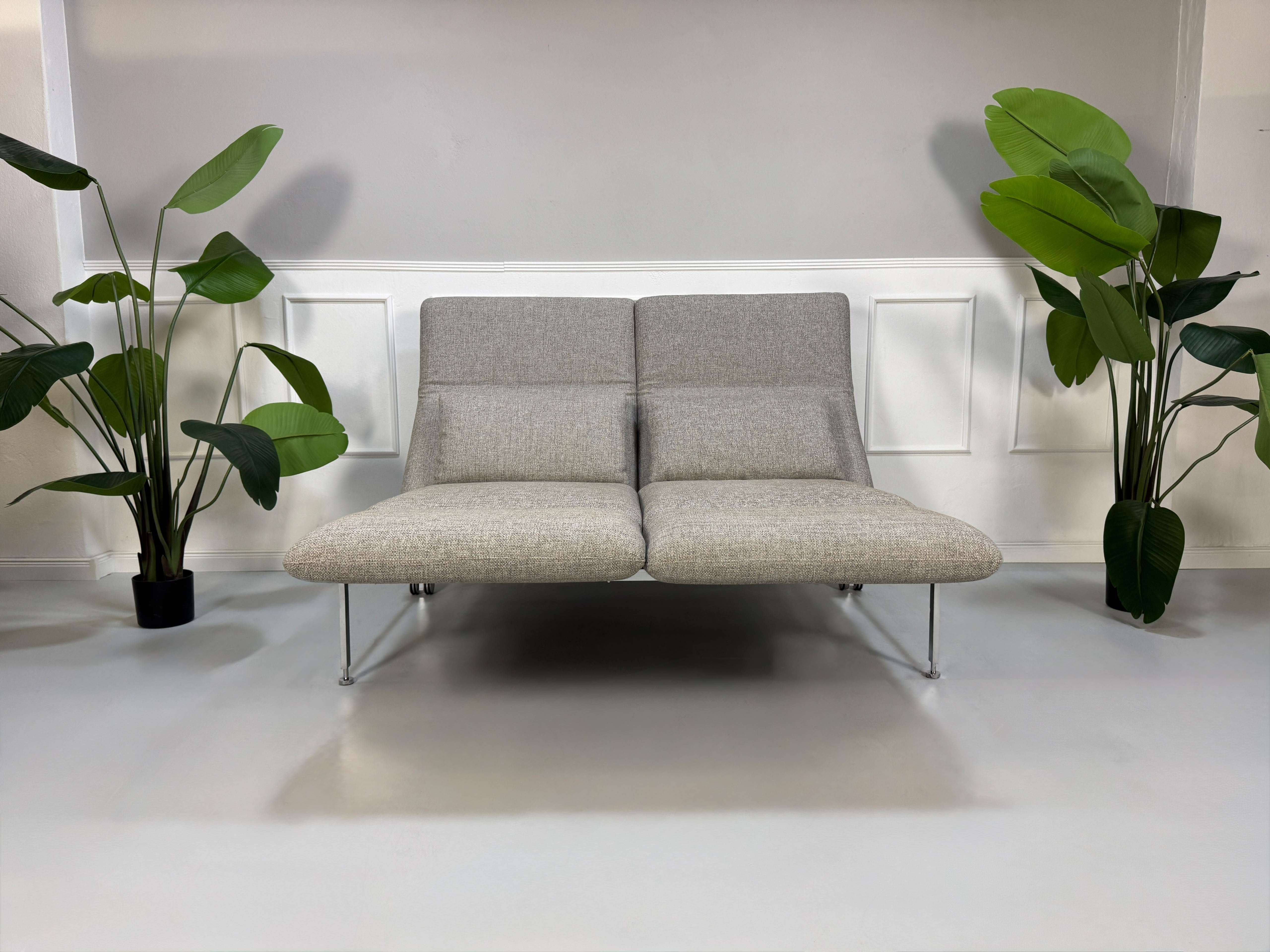 Fabrikverkauf Brühl Roro Designer Stoff Sofa vor einer Wand, stilvoll und modern eingerichtet.
