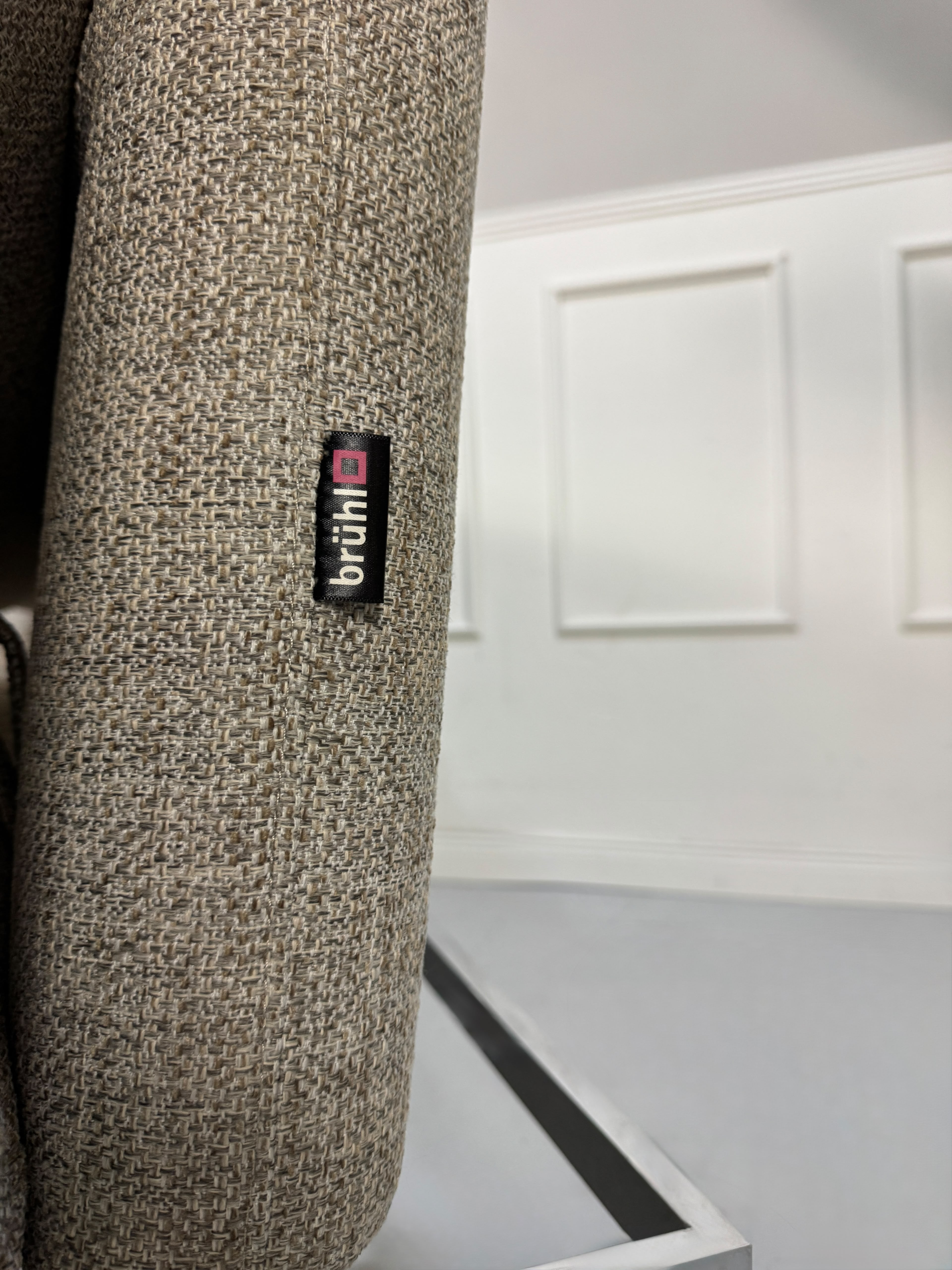Fabrikverkauf Brühl Roro Designer Stoff Sofa vor einer Wand, stilvoll und modern eingerichtet.