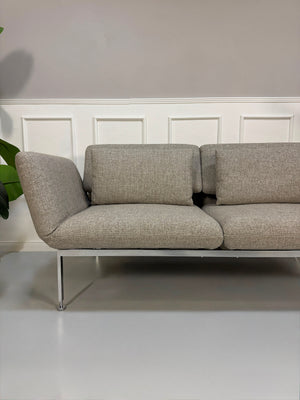 Fabrikverkauf Brühl Roro Designer Stoff Sofa vor einer Wand, stilvoll und modern eingerichtet.