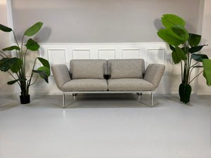 Fabrikverkauf Brühl Roro Designer Stoff Sofa vor einer Wand, stilvoll und modern eingerichtet.