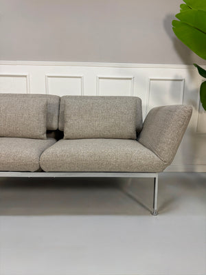 Fabrikverkauf Brühl Roro Designer Stoff Sofa vor einer Wand, stilvoll und modern eingerichtet.