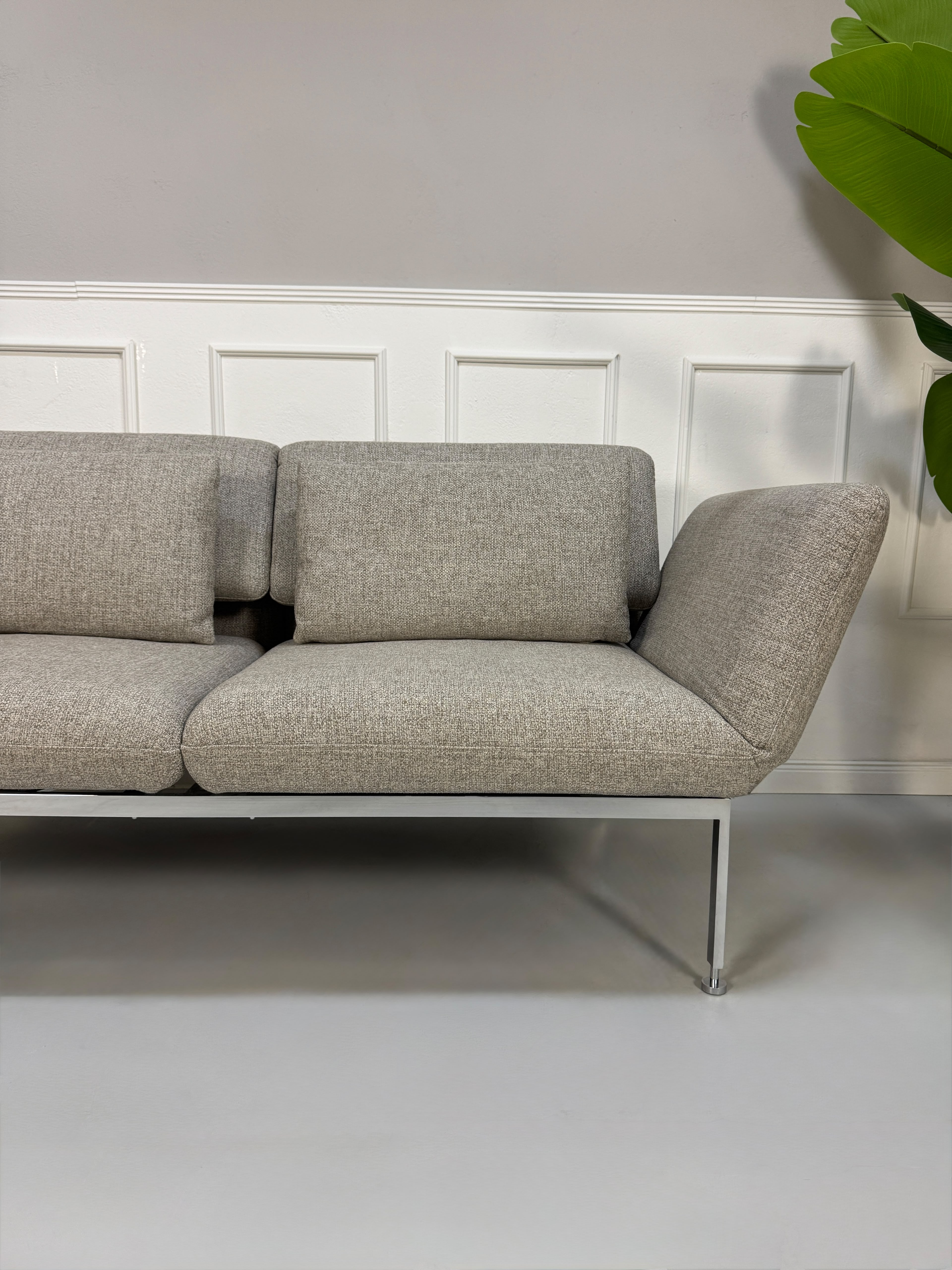 Fabrikverkauf Brühl Roro Designer Stoff Sofa vor einer Wand, stilvoll und modern eingerichtet.