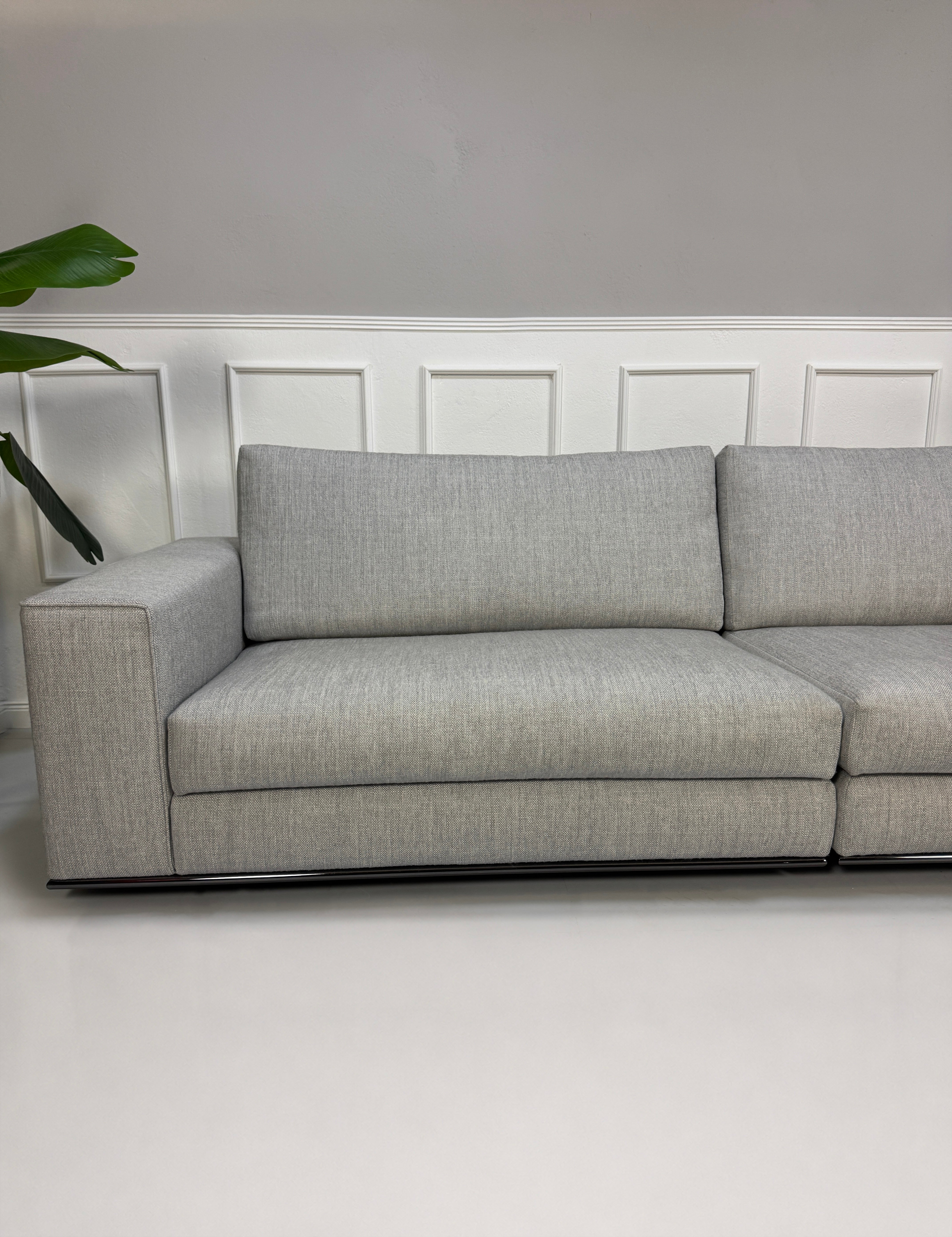 Ausstellungsstück graues Minotti Hamilton Designer Stoff Sofa vor einer Wand, stilvoll und modern eingerichtet.