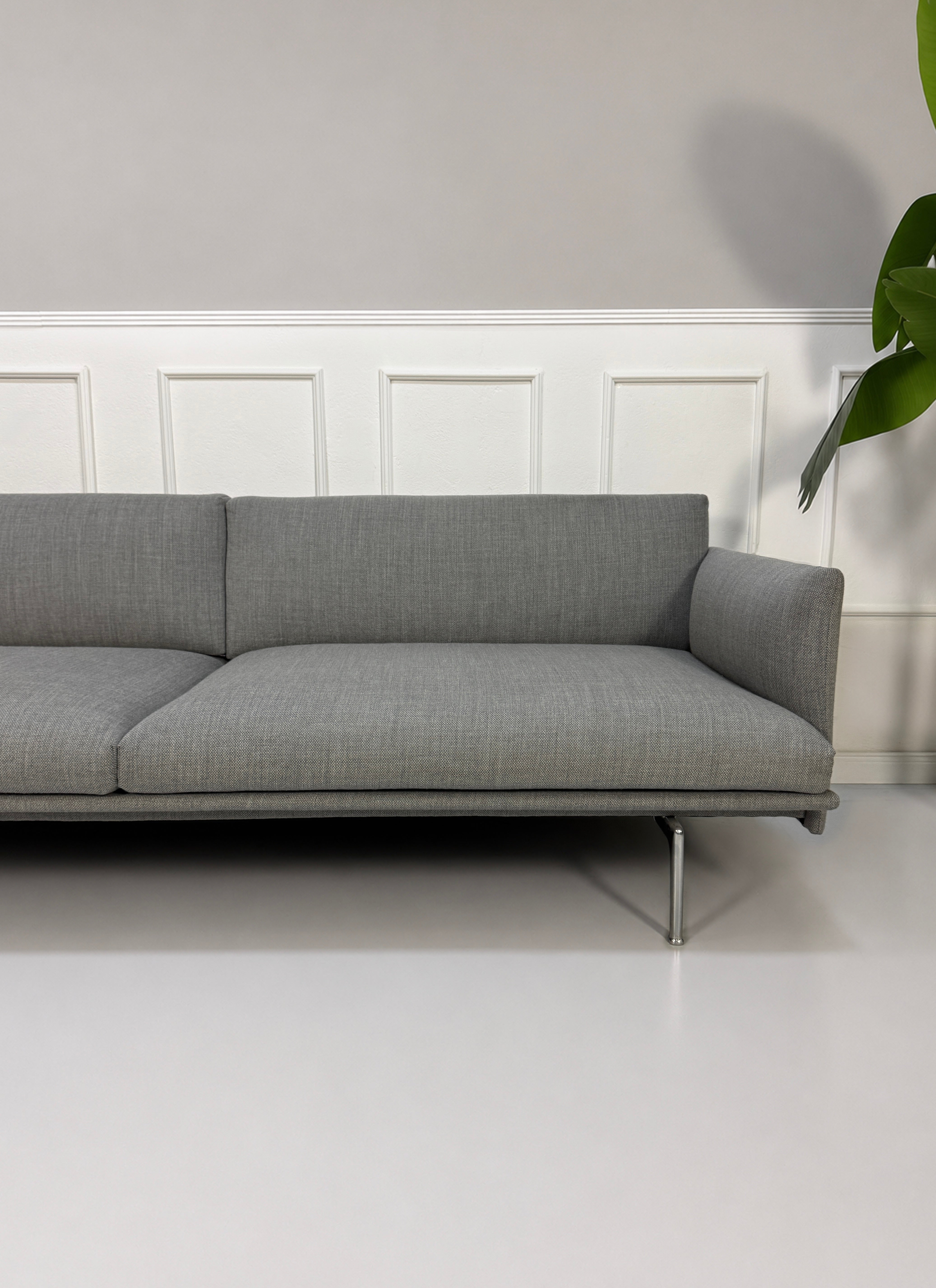 Gebrauchtes graues Muuto Outline Designer Stoff Sofa vor einer Wand, stilvoll und modern eingerichtet.