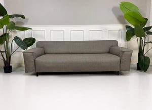 Gebrauchtes graues Rolf Benz Grata Designer Stoff Sofa mit Hocker vor einer Wand, stilvoll und modern eingerichtet.