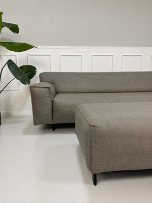 Gebrauchtes graues Rolf Benz Grata Designer Stoff Sofa mit Hocker vor einer Wand, stilvoll und modern eingerichtet.
