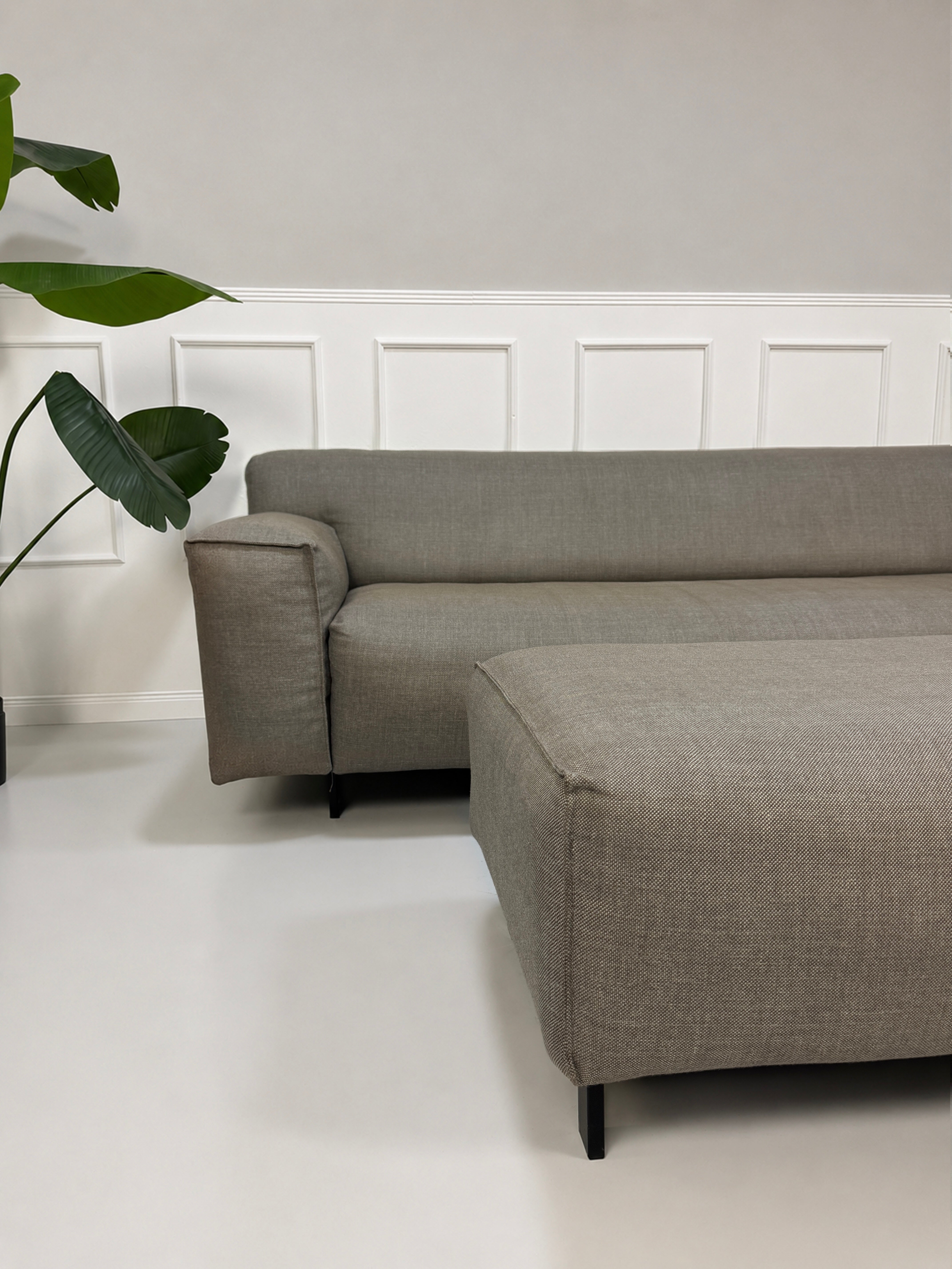 Gebrauchtes graues Rolf Benz Grata Designer Stoff Sofa mit Hocker vor einer Wand, stilvoll und modern eingerichtet.