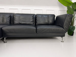 Gebrauchtes schwarzes Brühl Moule Designer Leder Sofa vor einer Wand, stilvoll und modern eingerichtet.