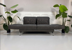 Gebrauchtes graues Brühl Moule Designer Stoff Sofa vor einer Wand, stilvoll und modern eingerichtet.