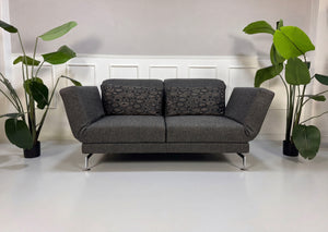 Gebrauchtes graues Brühl Moule Designer Stoff Sofa vor einer Wand, stilvoll und modern eingerichtet.