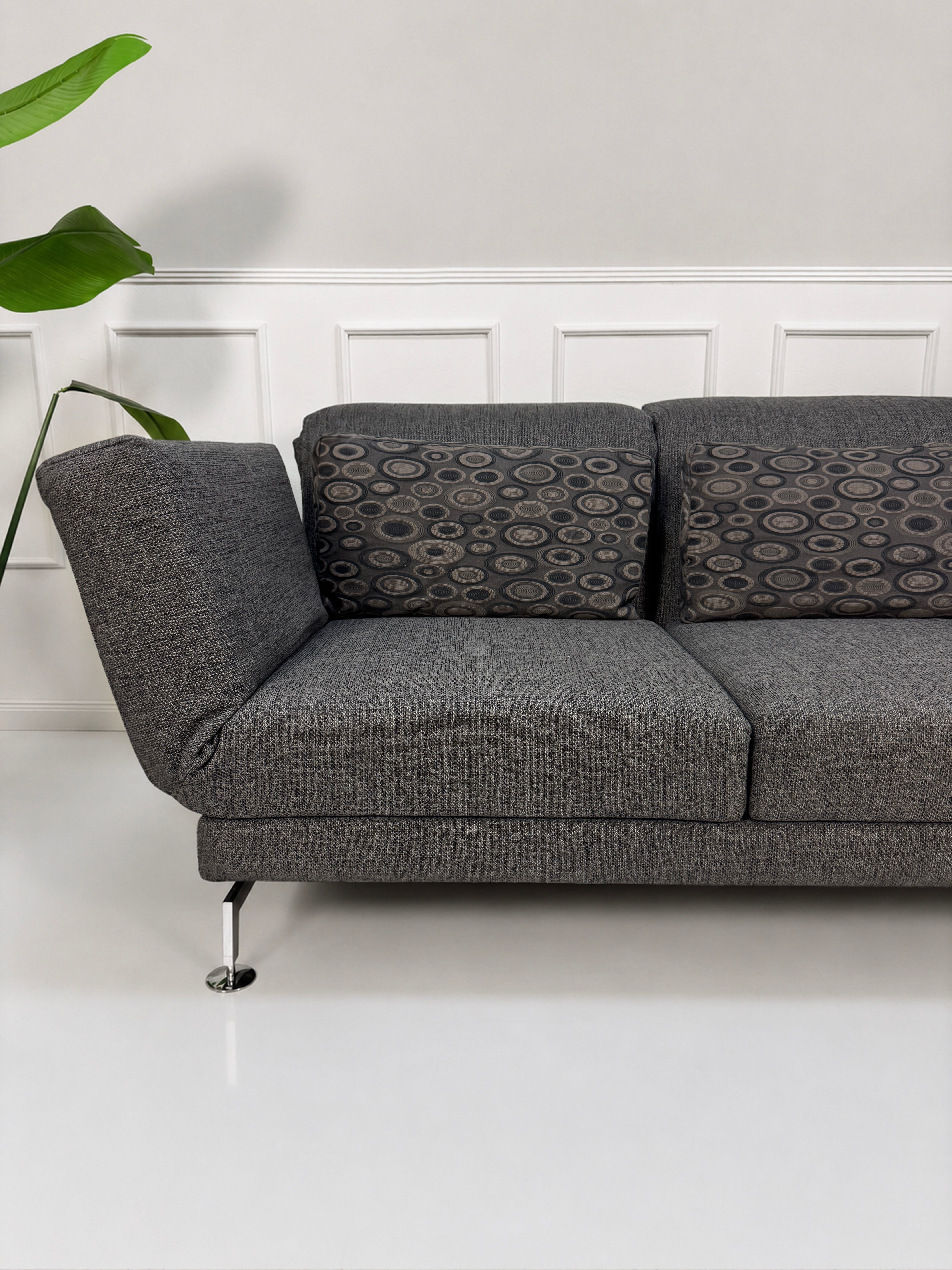 Gebrauchtes graues Brühl Moule Designer Stoff Sofa vor einer Wand, stilvoll und modern eingerichtet.