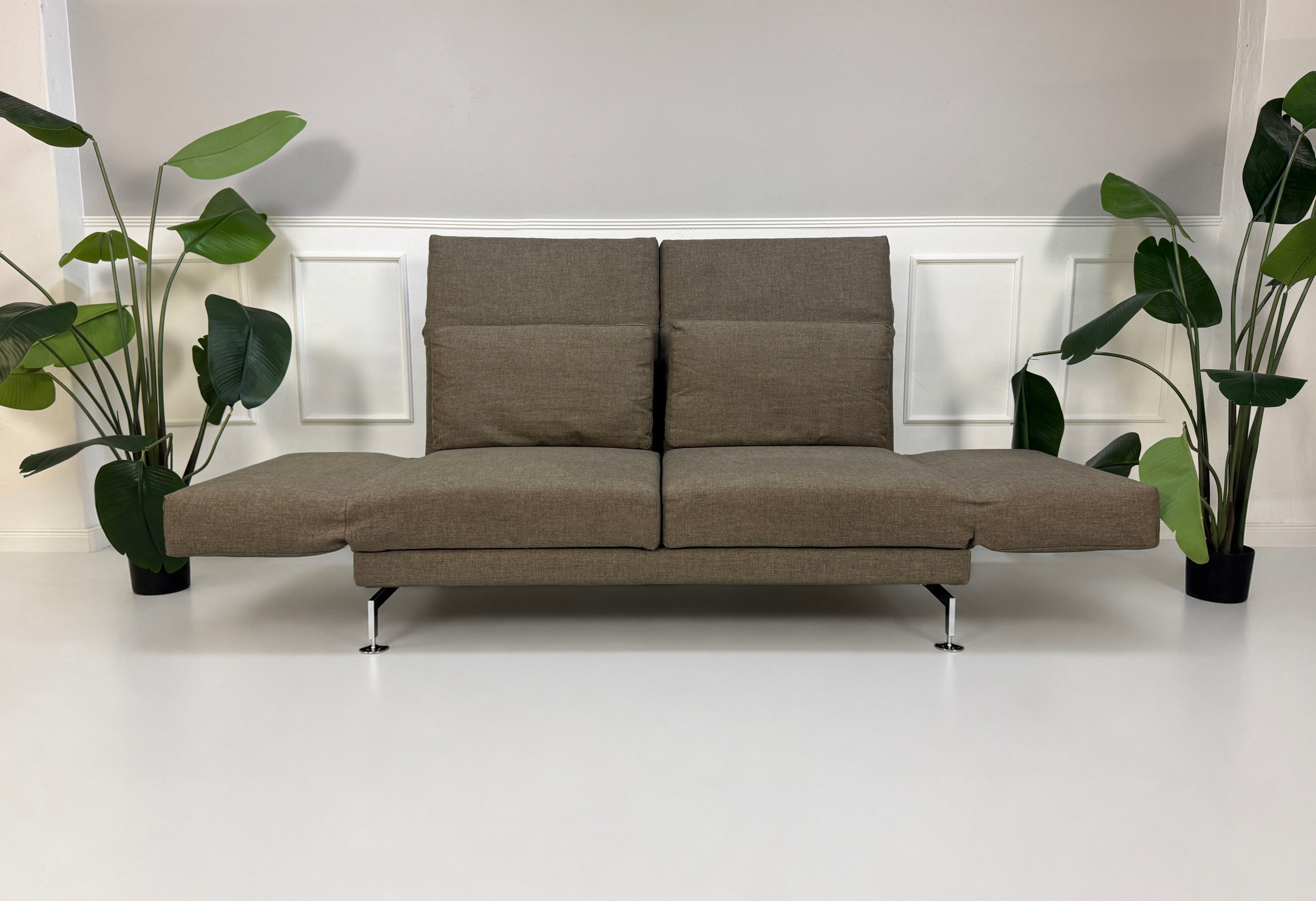 Gebrauchtes braunes Brühl Moule Designer Stoff Sofa vor einer Wand, stilvoll und modern eingerichtet.