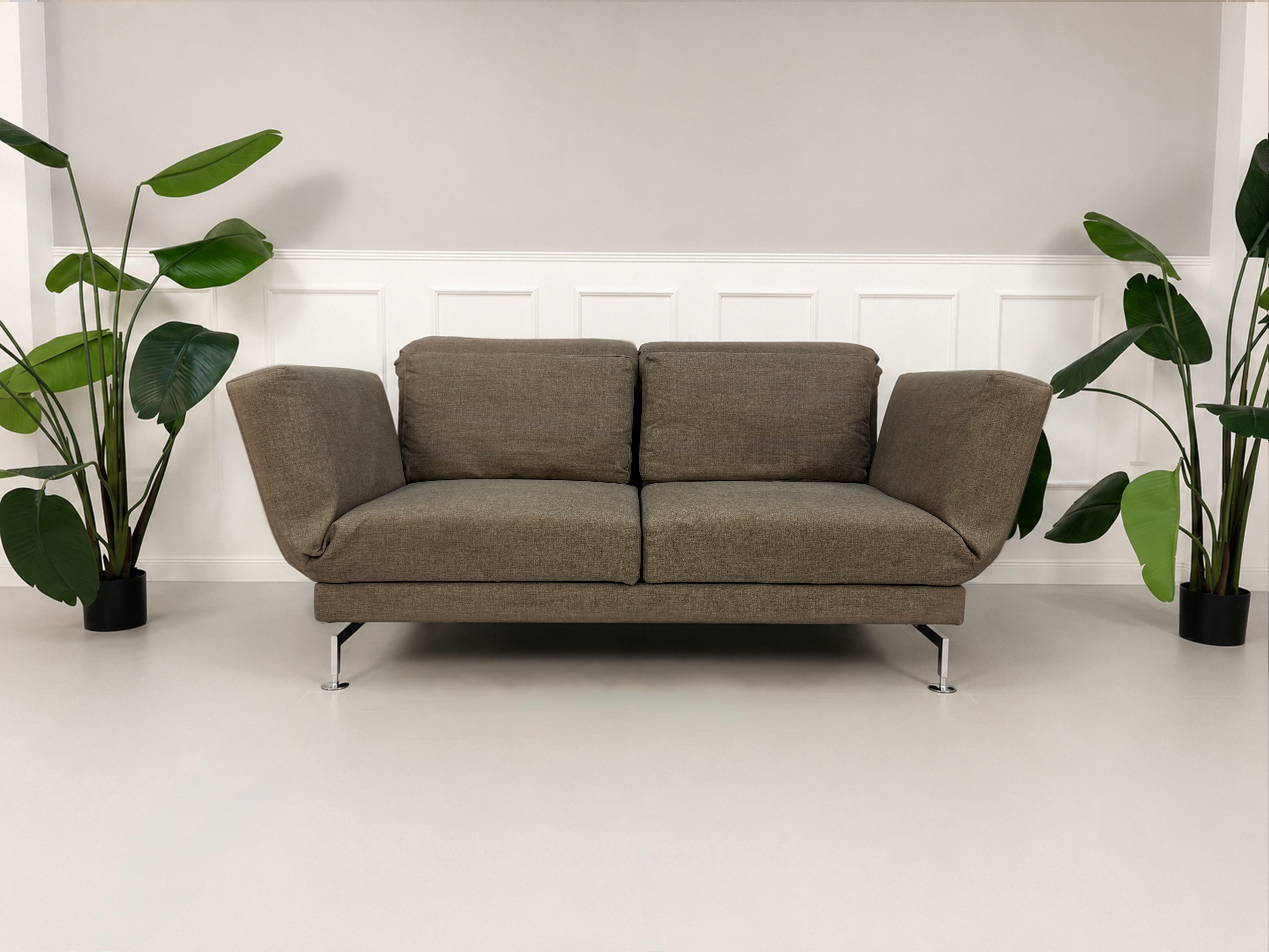 Gebrauchtes braunes Brühl Moule Designer Stoff Sofa vor einer Wand, stilvoll und modern eingerichtet.