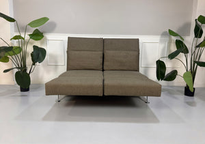 Gebrauchtes braunes Brühl Moule Designer Stoff Sofa vor einer Wand, stilvoll und modern eingerichtet.
