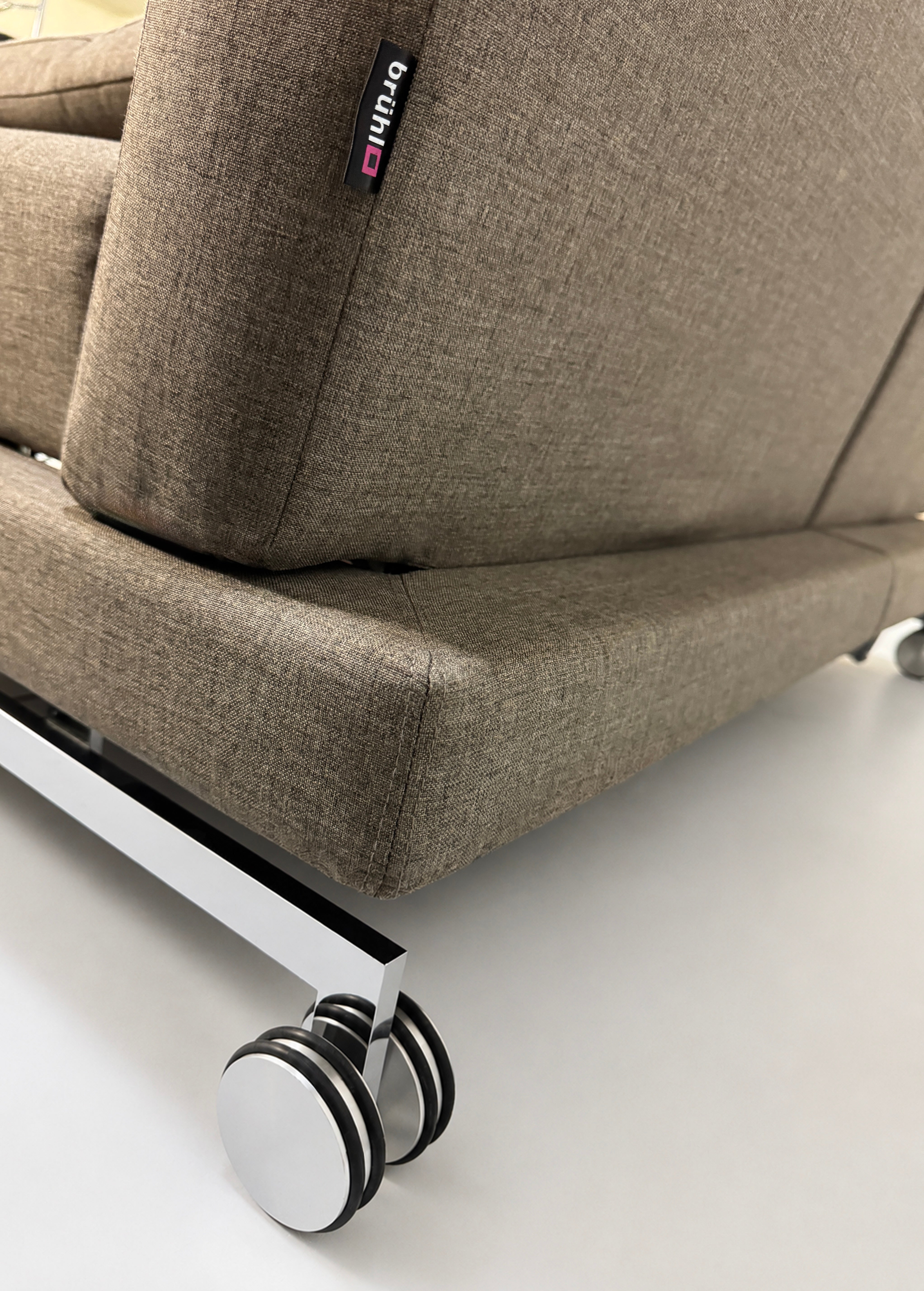 Gebrauchtes braunes Brühl Moule Designer Stoff Sofa vor einer Wand, stilvoll und modern eingerichtet.