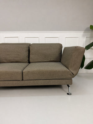 Gebrauchtes braunes Brühl Moule Designer Stoff Sofa vor einer Wand, stilvoll und modern eingerichtet.