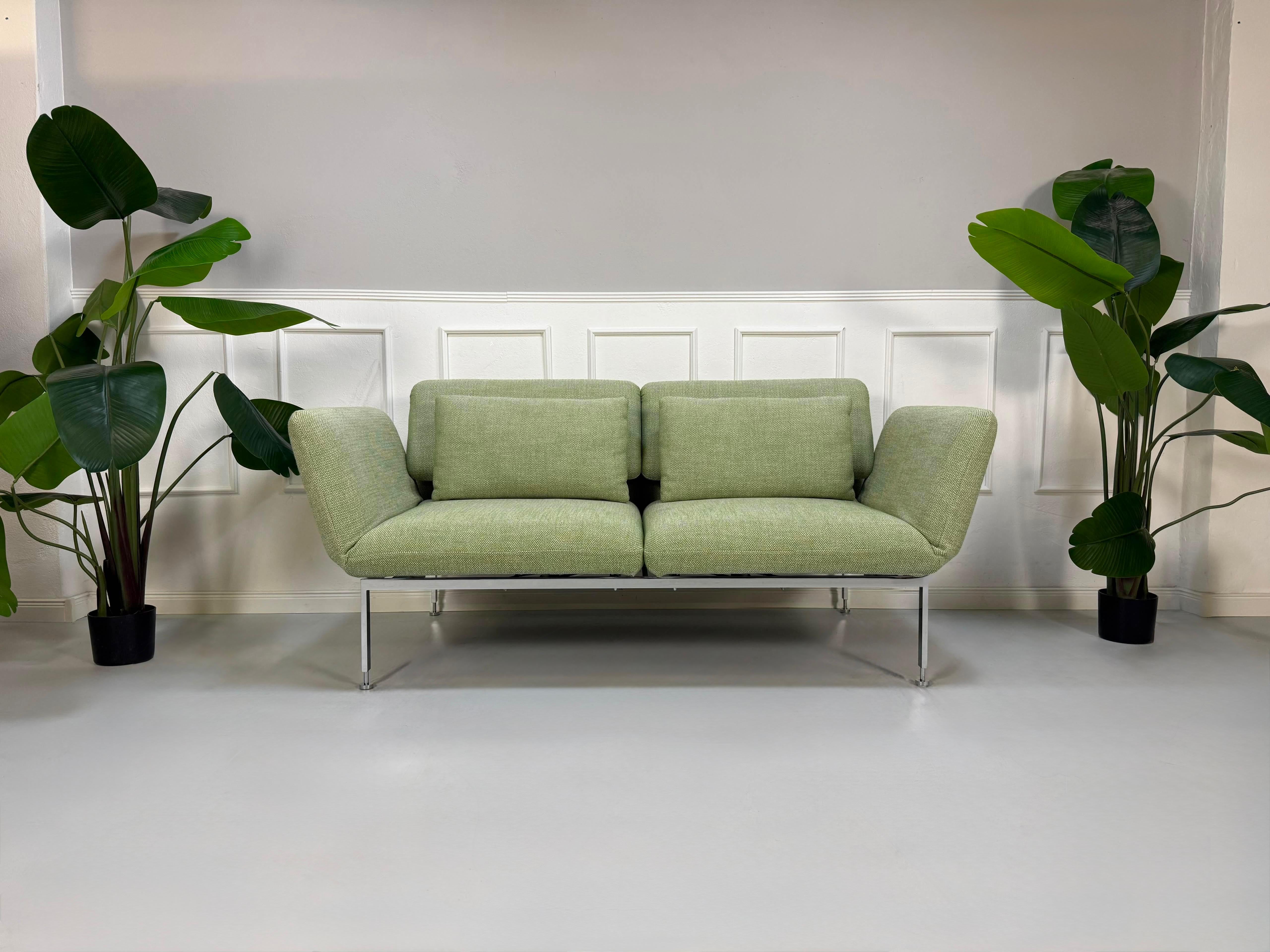 Fabrikverkauf grünes Brühl Roro Designer Stoff Sofa vor einer Wand, stilvoll und modern eingerichtet.