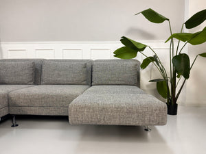 Gebrauchtes graues Brühl Designer Stoff Sofa vor einer Wand, stilvoll und modern eingerichtet.