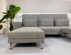 Gebrauchtes graues Brühl Designer Stoff Sofa vor einer Wand, stilvoll und modern eingerichtet.