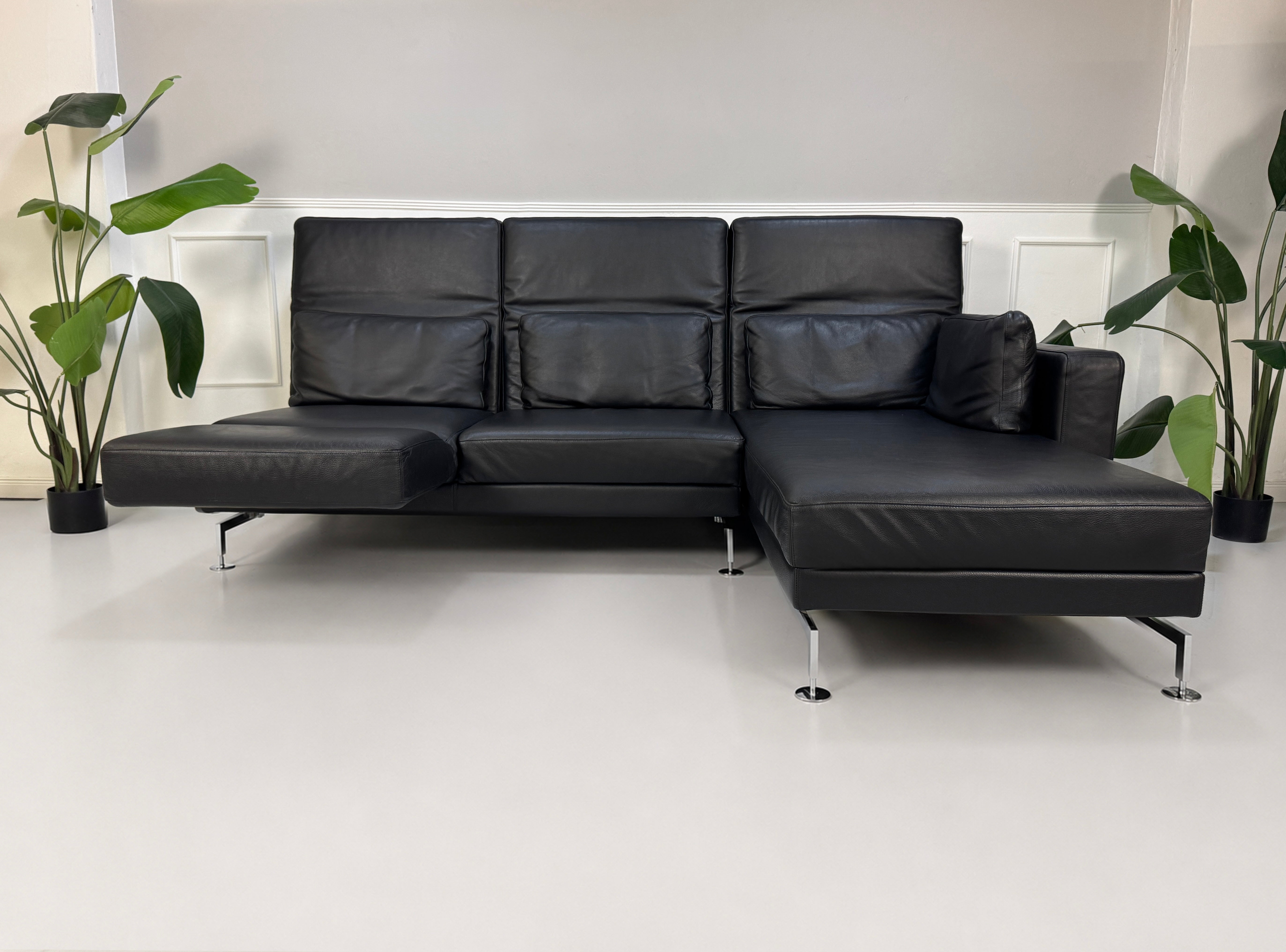 Gebrauchtes schwarzes Brühl Moule Designer Leder Sofa vor einer Wand, stilvoll und modern eingerichtet.