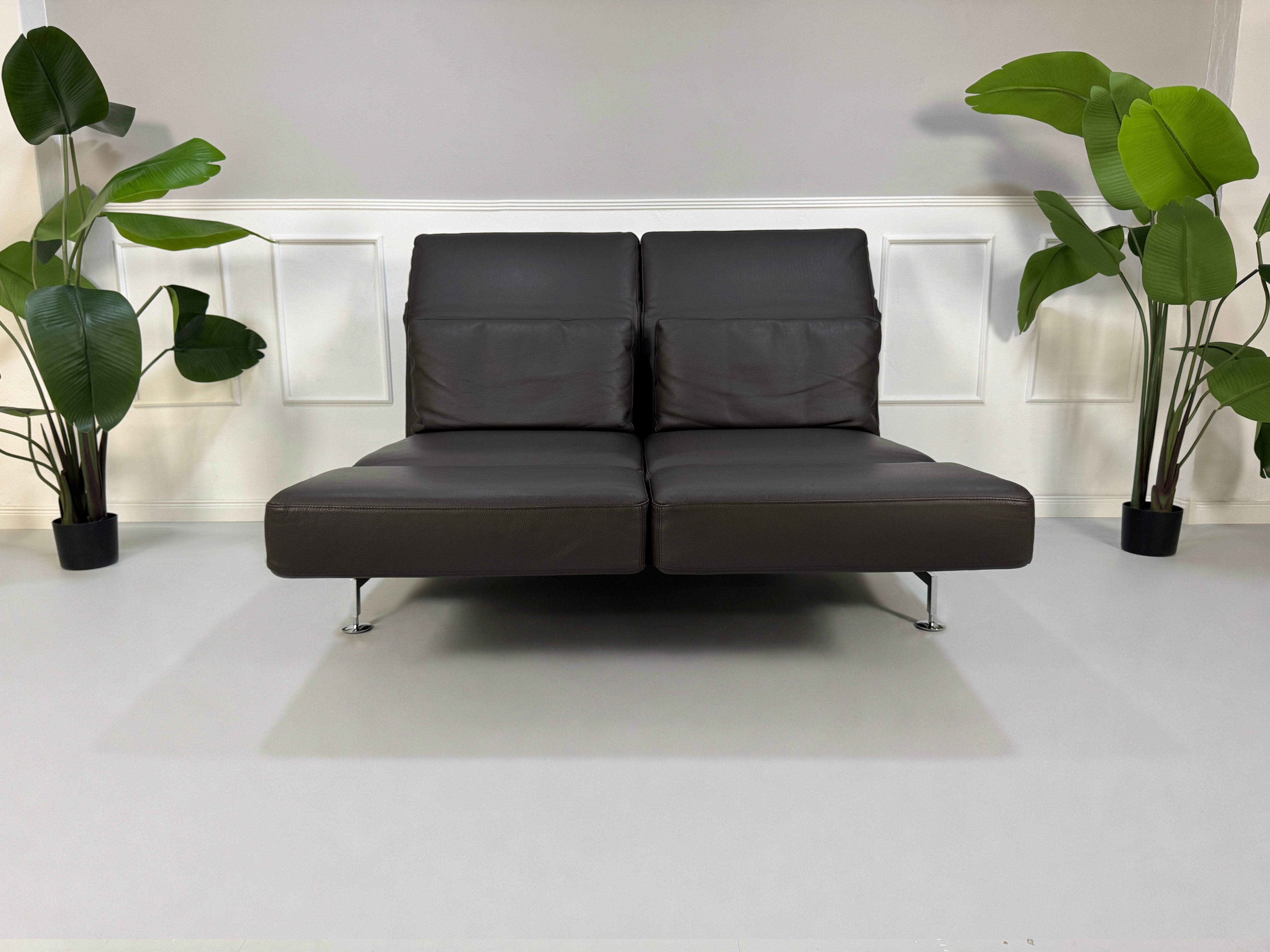 Gebrauchtes braunes Brühl Moule Designer Leder Sofa vor einer Wand, stilvoll und modern eingerichtet.