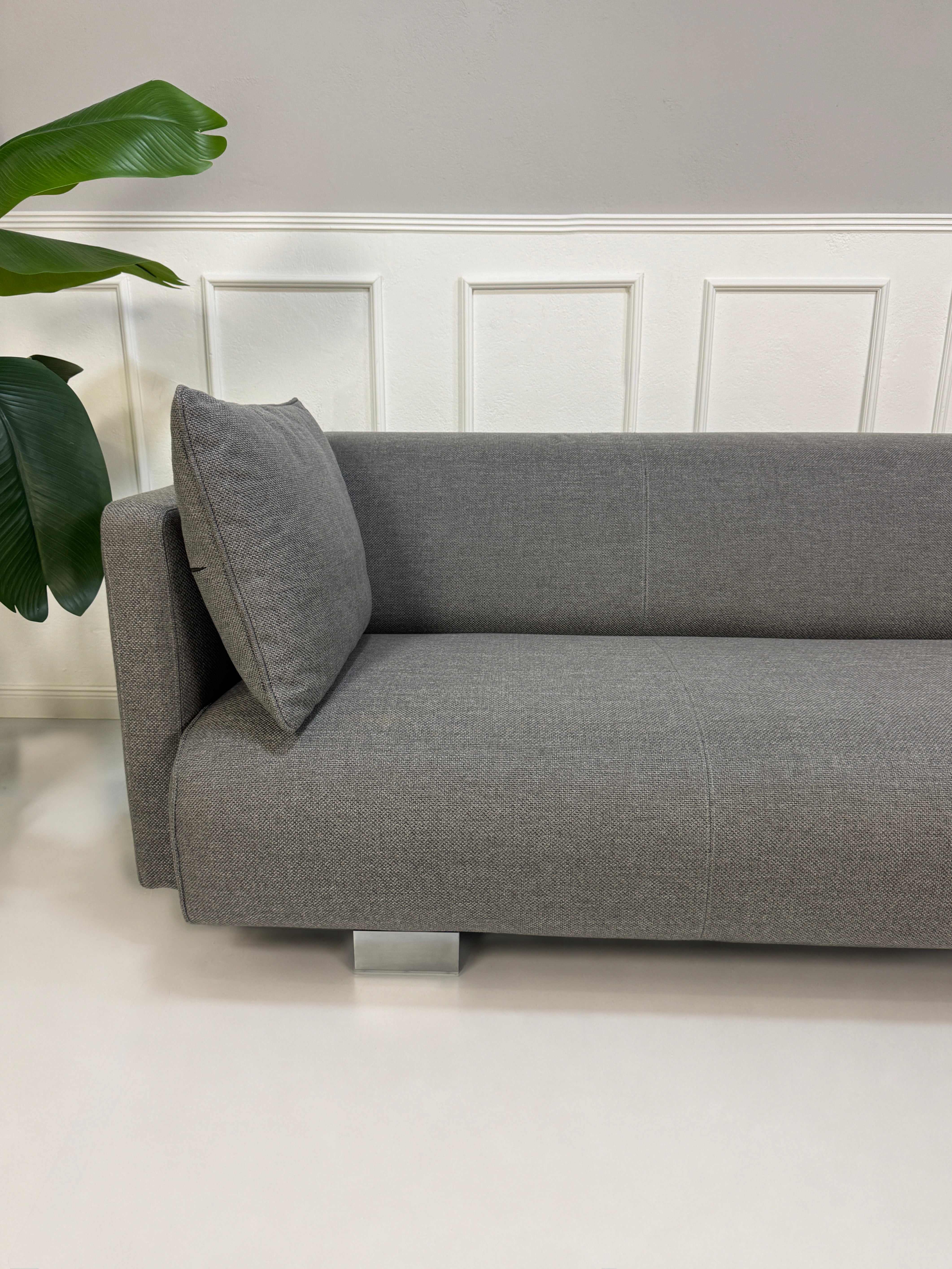 Gebrauchtes graues Rolf Benz 6300 Designer Stoff Sofa vor einer Wand, stilvoll und modern eingerichtet.