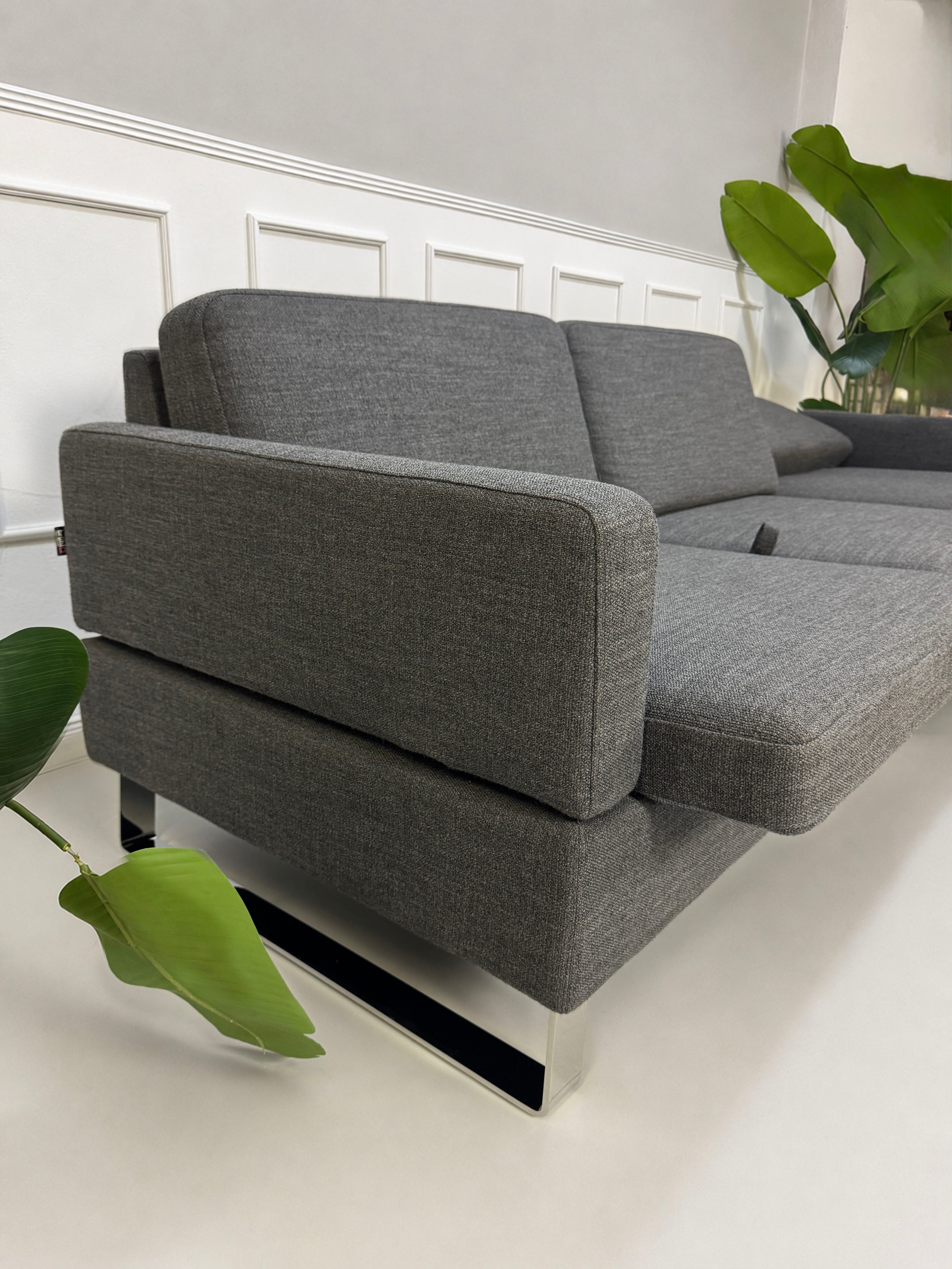 Gebrauchtes graues Brühl Alba Designer Stoff Sofa vor einer Wand, stilvoll und modern eingerichtet.