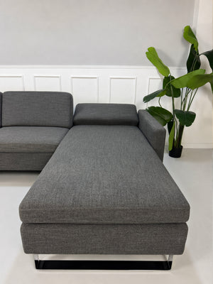 Gebrauchtes graues Brühl Alba Designer Stoff Sofa vor einer Wand, stilvoll und modern eingerichtet.