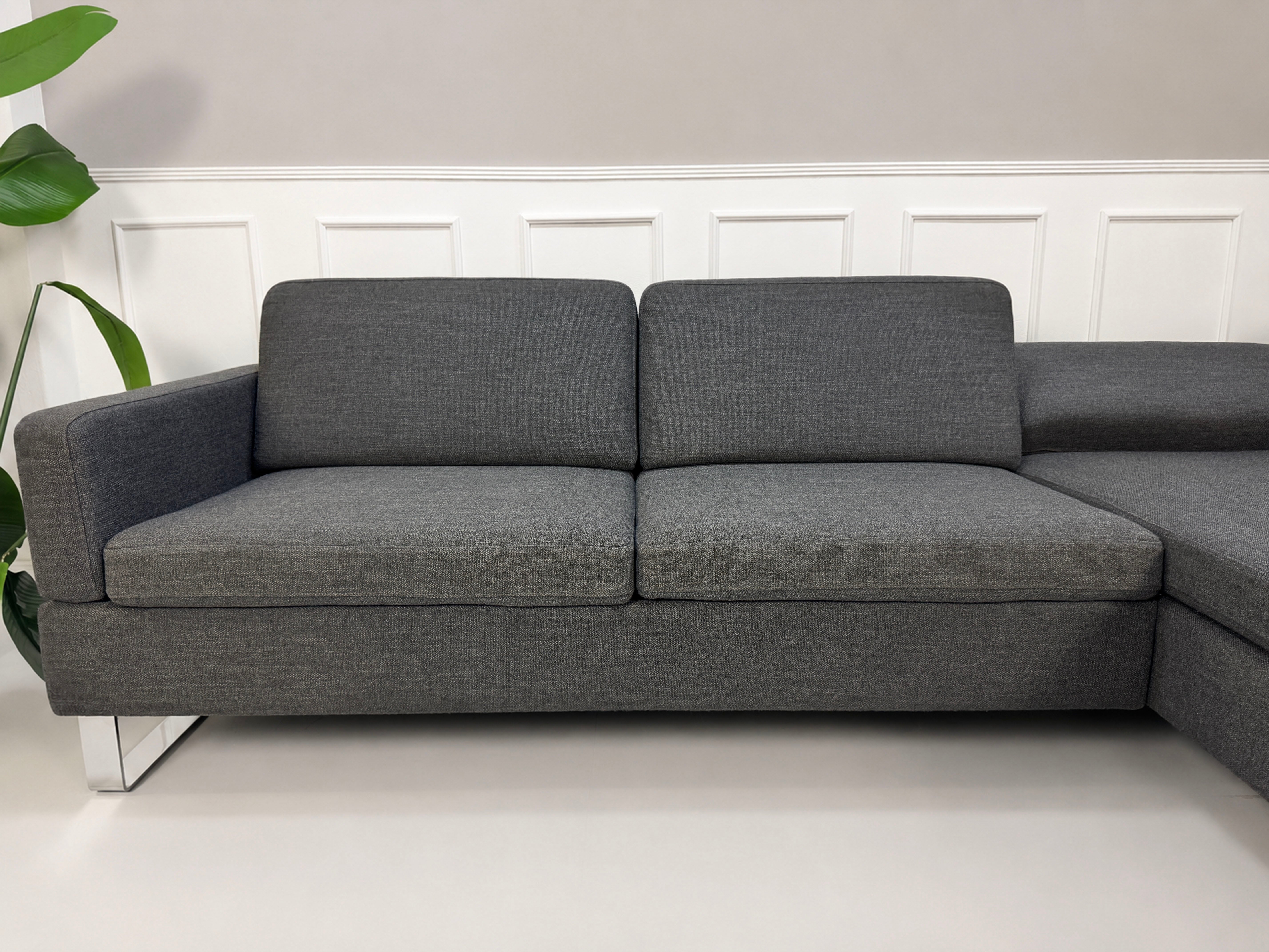Gebrauchtes graues Brühl Alba Designer Stoff Sofa vor einer Wand, stilvoll und modern eingerichtet.