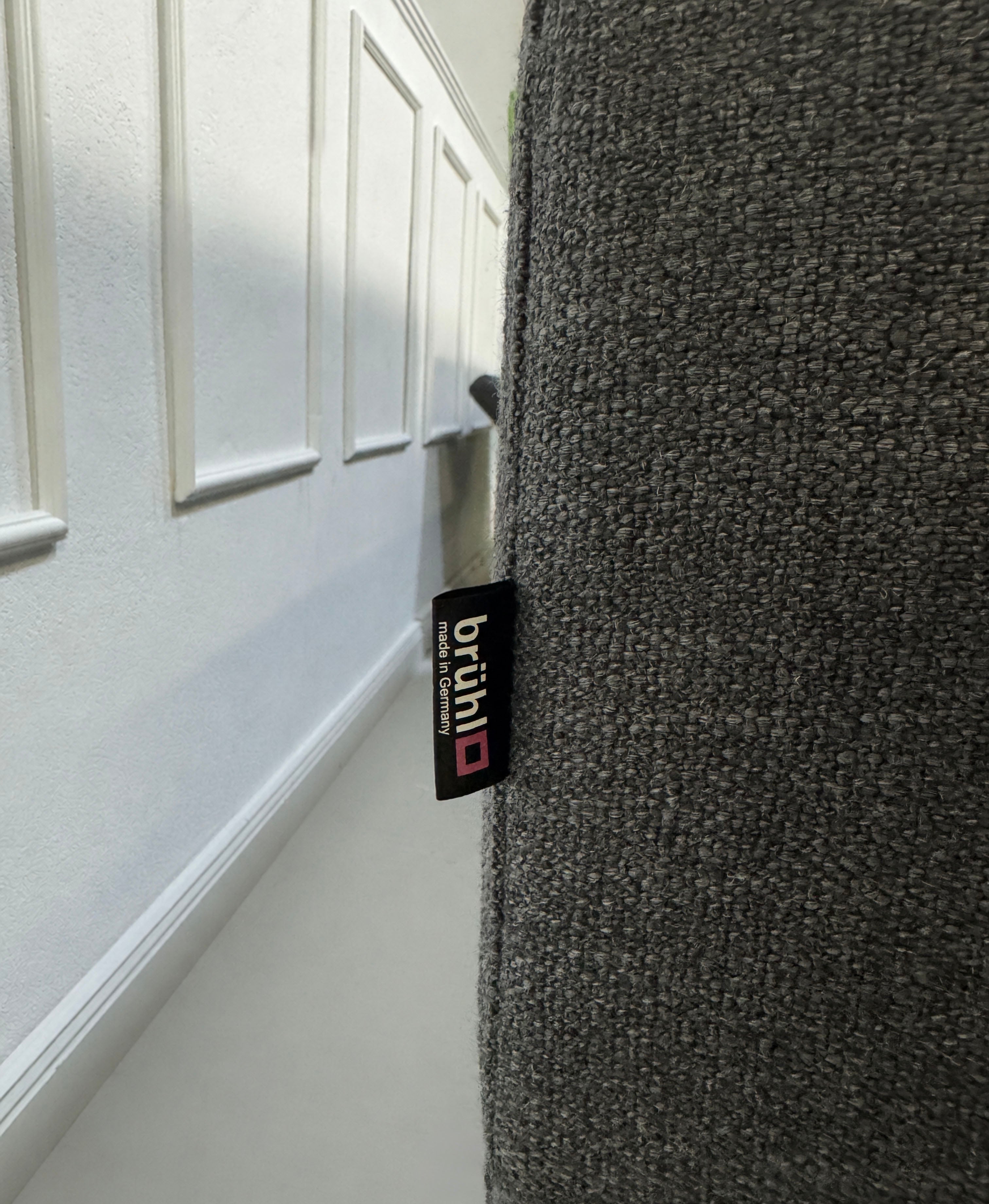 Gebrauchtes graues Brühl Alba Designer Stoff Sofa vor einer Wand, stilvoll und modern eingerichtet.