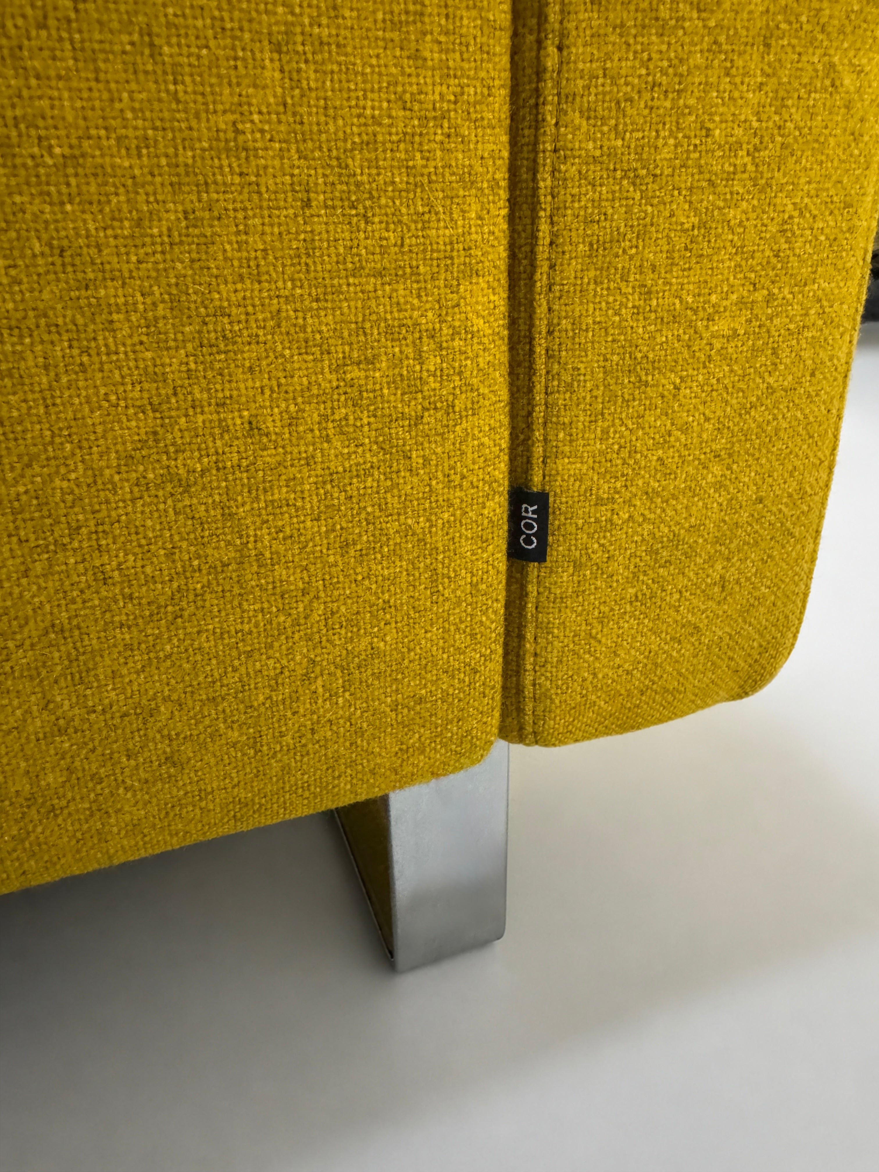 Gelbes Ausstellungsstück COR Conseta Designer Stoff Sofa vor einer Wand, stilvoll und modern eingerichtet.