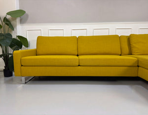 Gelbes Ausstellungsstück COR Conseta Designer Stoff Sofa vor einer Wand, stilvoll und modern eingerichtet.