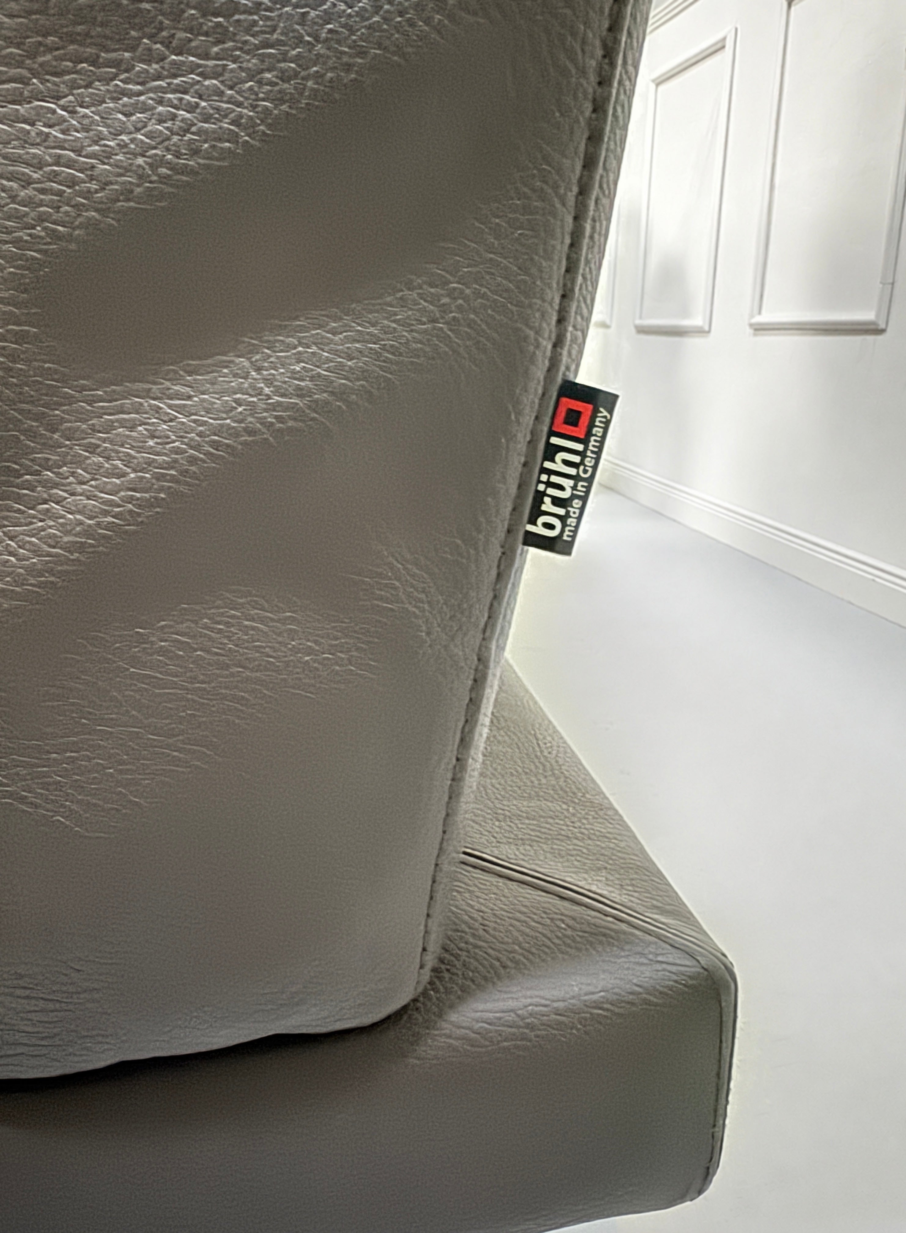 Gebrauchtes braunes Brühl Moule Designer Leder Sofa vor einer Wand, stilvoll und modern eingerichtet.