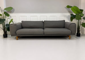 Gebrauchtes graues Muuto Rest Designer Stoff Sofa mit Hocker vor einer Wand, stilvoll und modern eingerichtet.
