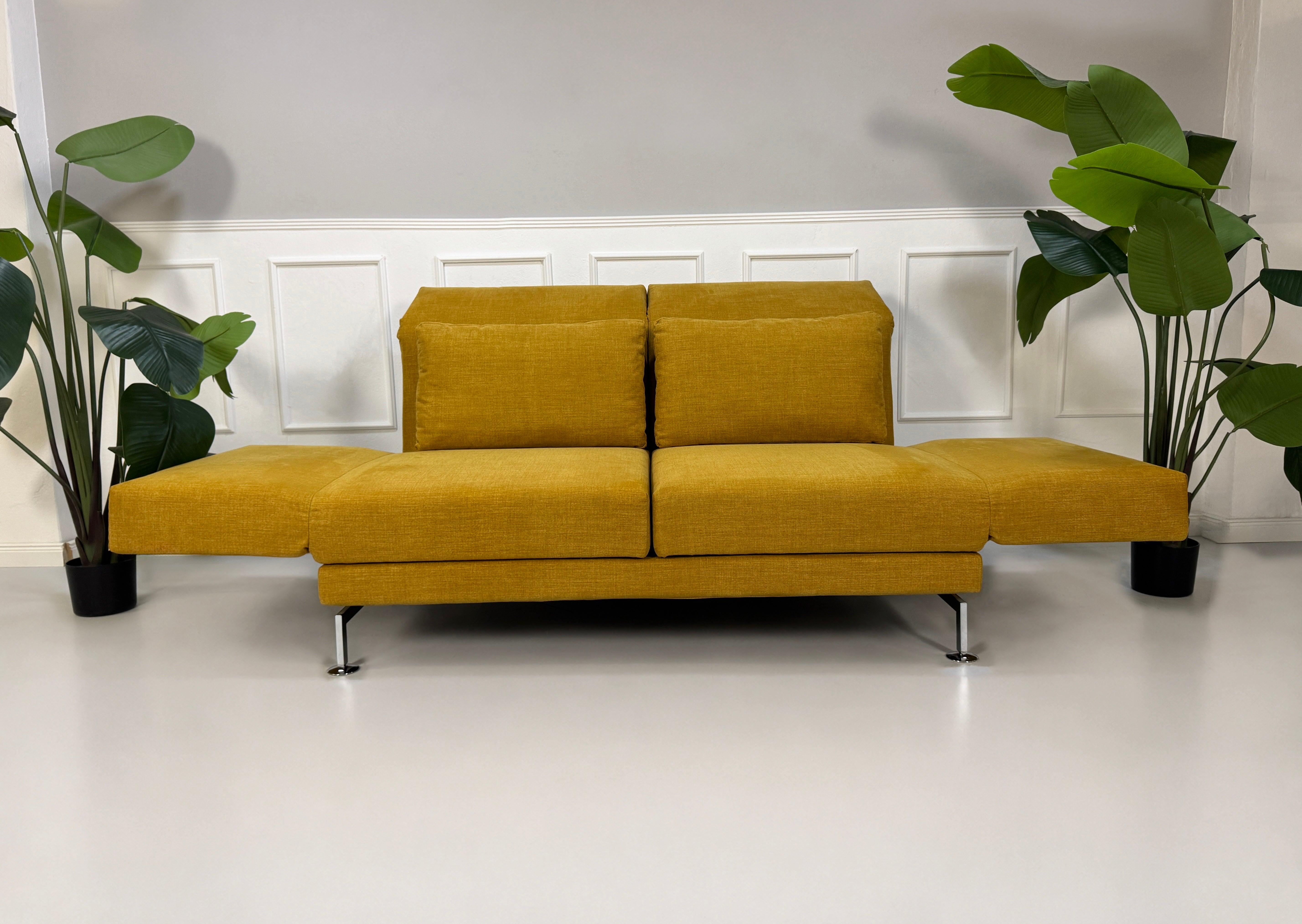 Gebrauchtes gelbes Brühl Moule Designer Stoff Sofa vor einer Wand, stilvoll und modern eingerichtet.