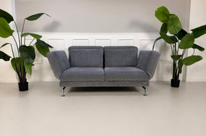 Gebrauchtes graues Brühl Moule Designer Stoff Sofa vor einer Wand, stilvoll und modern eingerichtet.