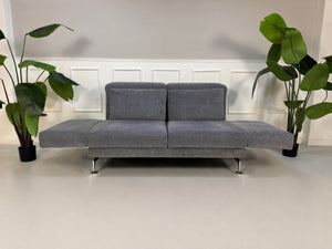 Gebrauchtes graues Brühl Moule Designer Stoff Sofa vor einer Wand, stilvoll und modern eingerichtet.