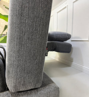 Gebrauchtes graues Brühl Moule Designer Stoff Sofa vor einer Wand, stilvoll und modern eingerichtet.