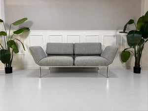 Gebrauchtes graues Brühl Roro Medium Designer Stoff Sofa vor einer Wand, stilvoll und modern eingerichtet.