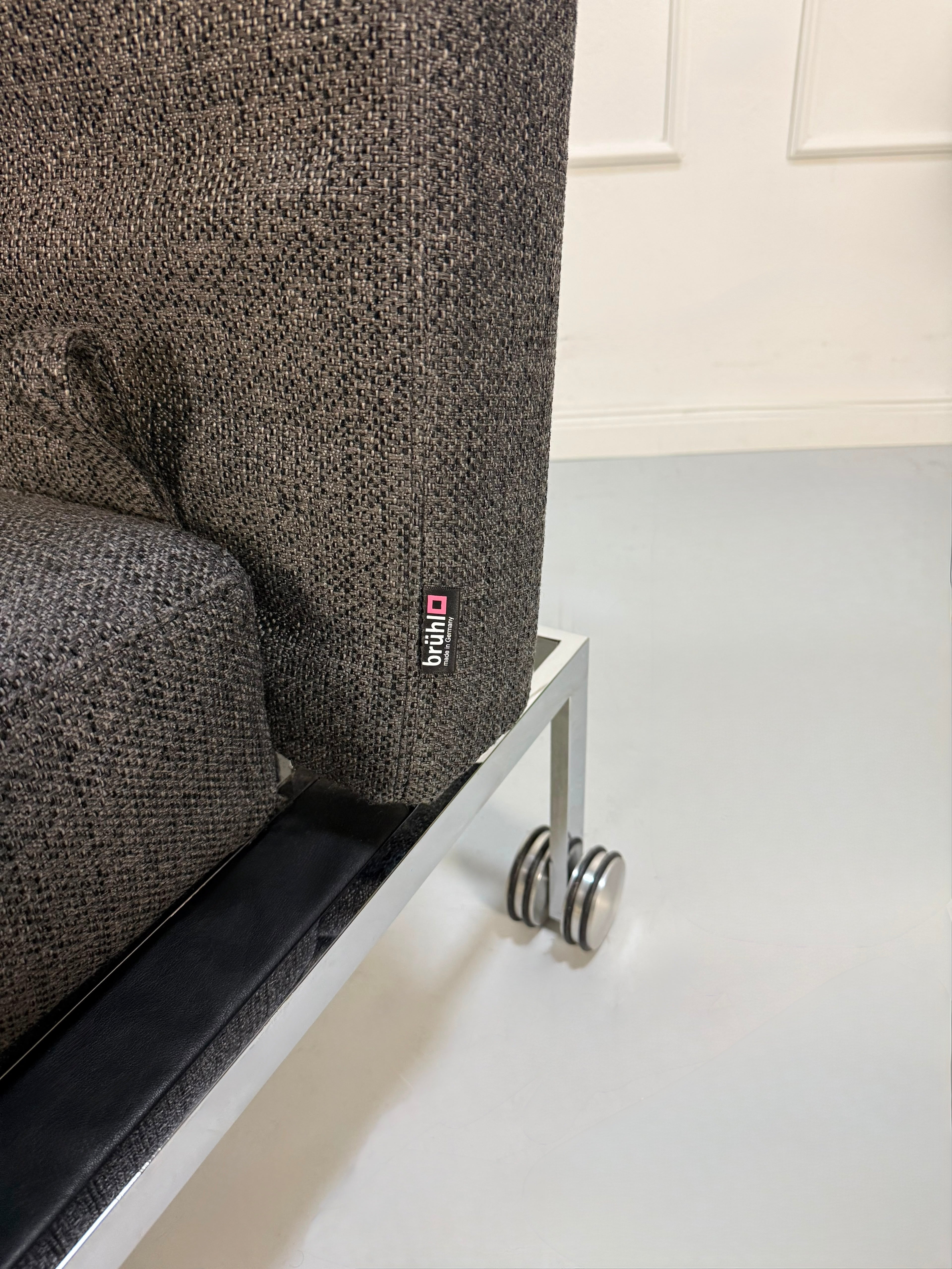 Gebrauchtes graues Brühl Roro Soft Designer Stoff Sofa vor einer Wand, stilvoll und modern eingerichtet.
